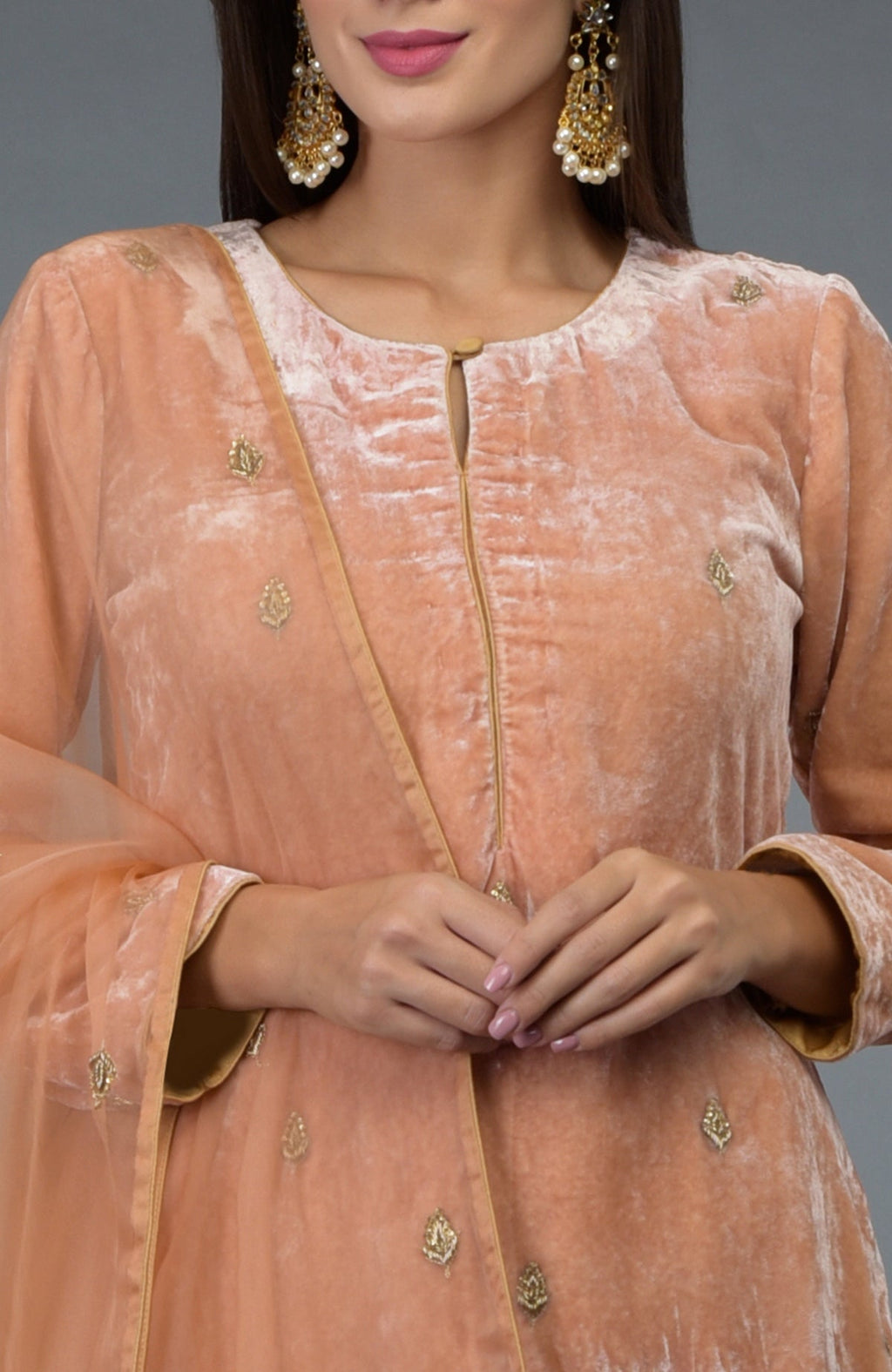 A woman models a peach rose silk velvet suit with gold embroidery and earrings.