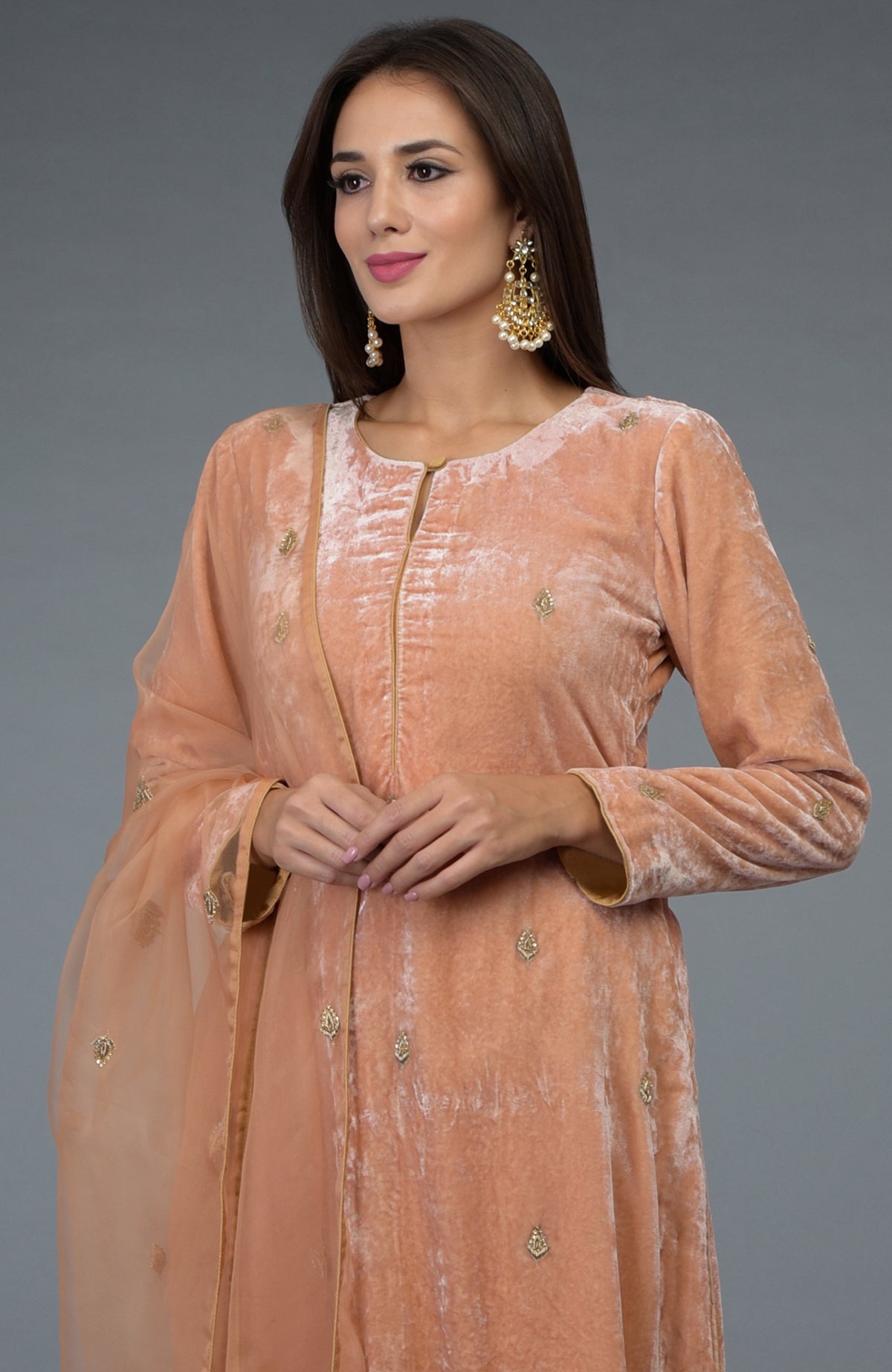 A woman models a peach rose zardozi hand-embroidered silk velvet suit.