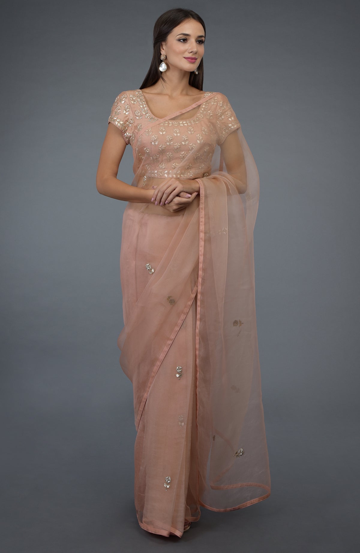 A woman models a pressed rose organza silk saree with zardozi and gota patti embroidery.