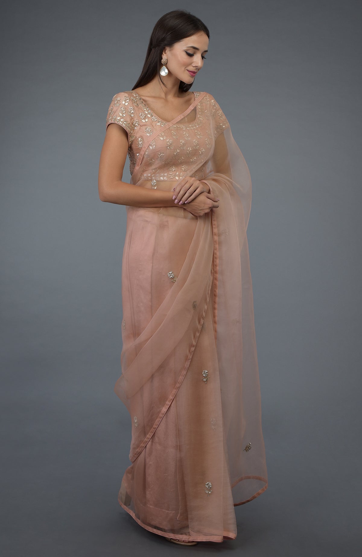 A woman models a pressed rose organza silk saree with zardozi and gota patti embroidery.