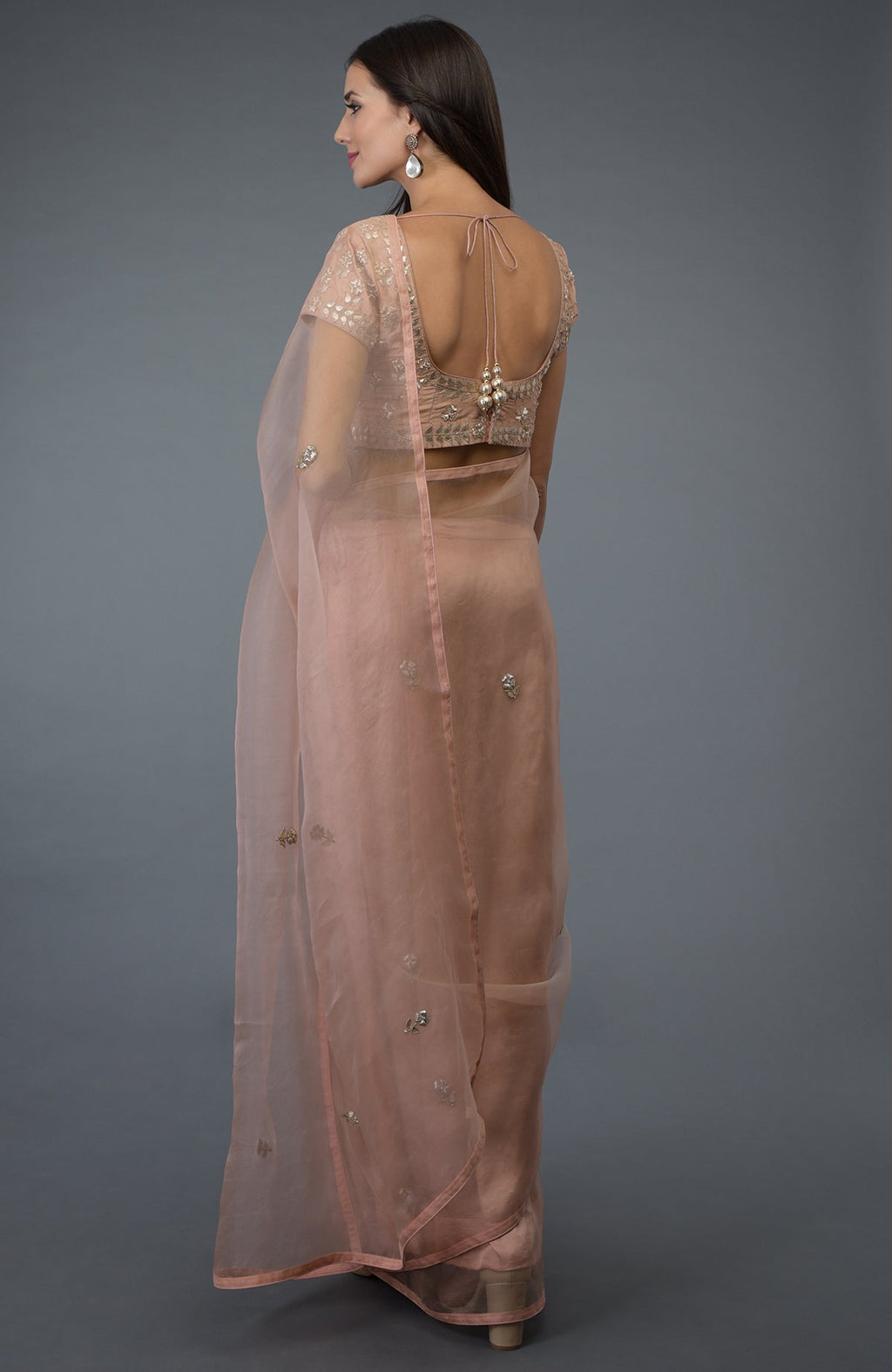 A woman models a pressed rose organza silk saree and blouse with zardozi embroidery.
