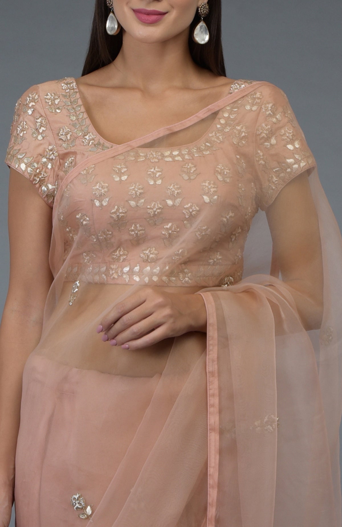 A woman models a pressed rose organza silk saree and blouse with zardozi embroidery.