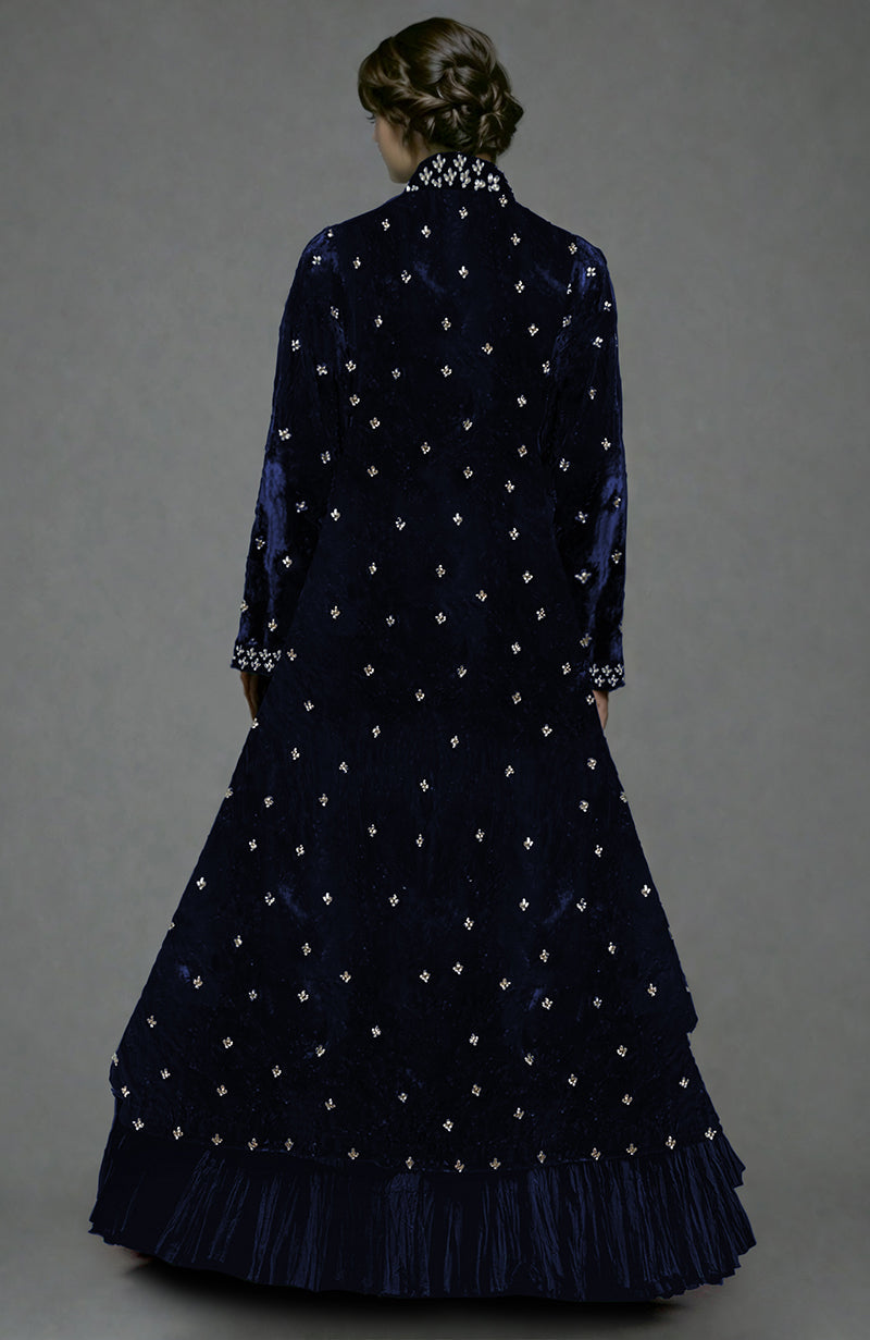 A woman from behind wears a midnight blue velvet jacket and tiered skirt with crystal embroidery.