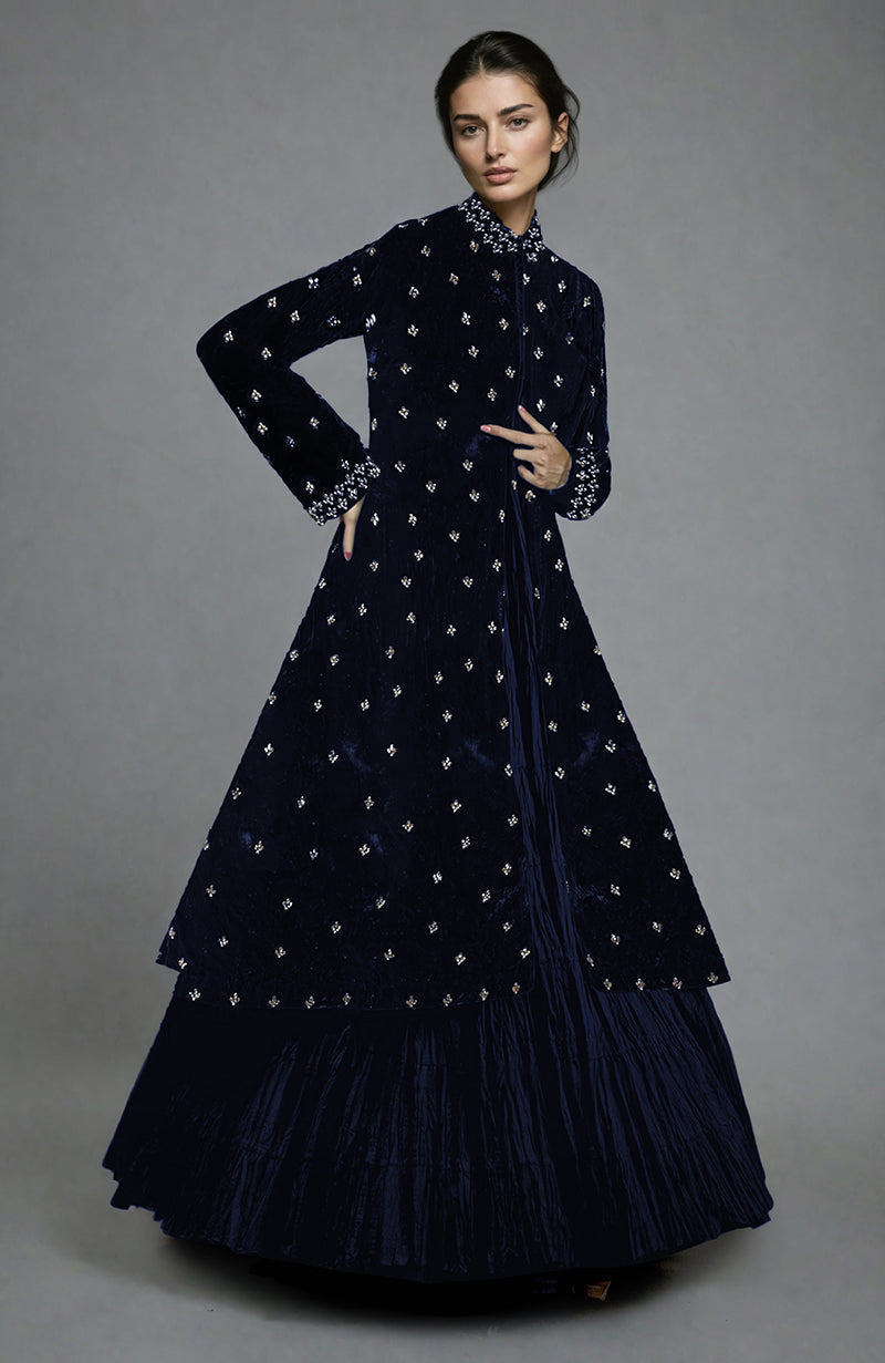 A model wears a midnight blue velvet jacket with crystal embroidery and a tiered skirt.
