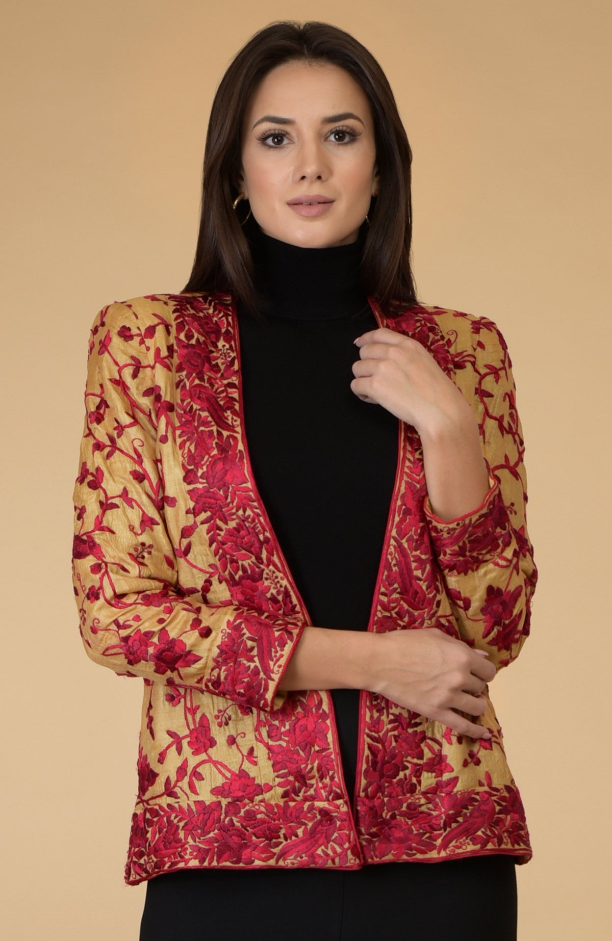 A woman models a fawn gold Parsi Gara embroidered tussar silk shrug jacket with red floral and bird embroidery.