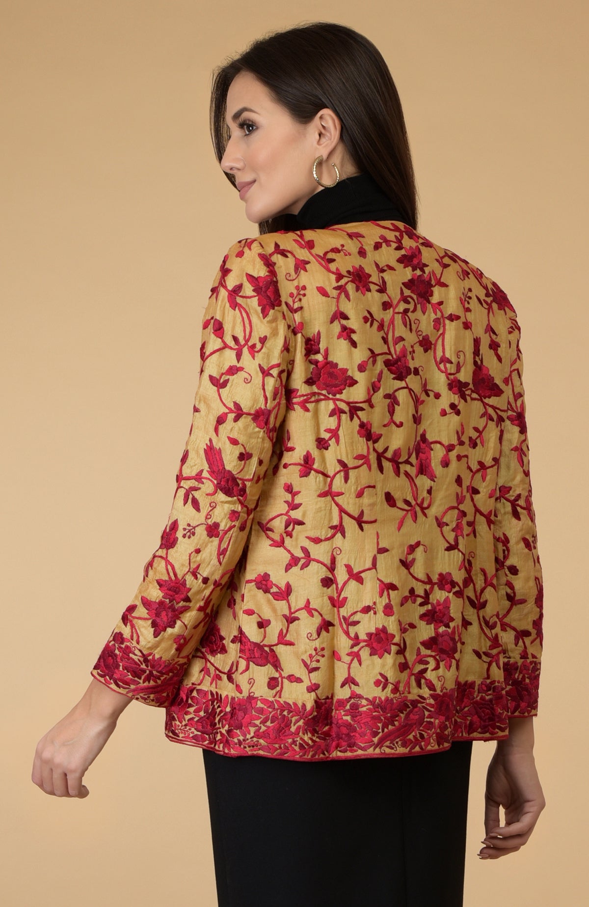 Woman in a fawn gold Parsi Gara embroidered shrug jacket with red floral and bird motifs.