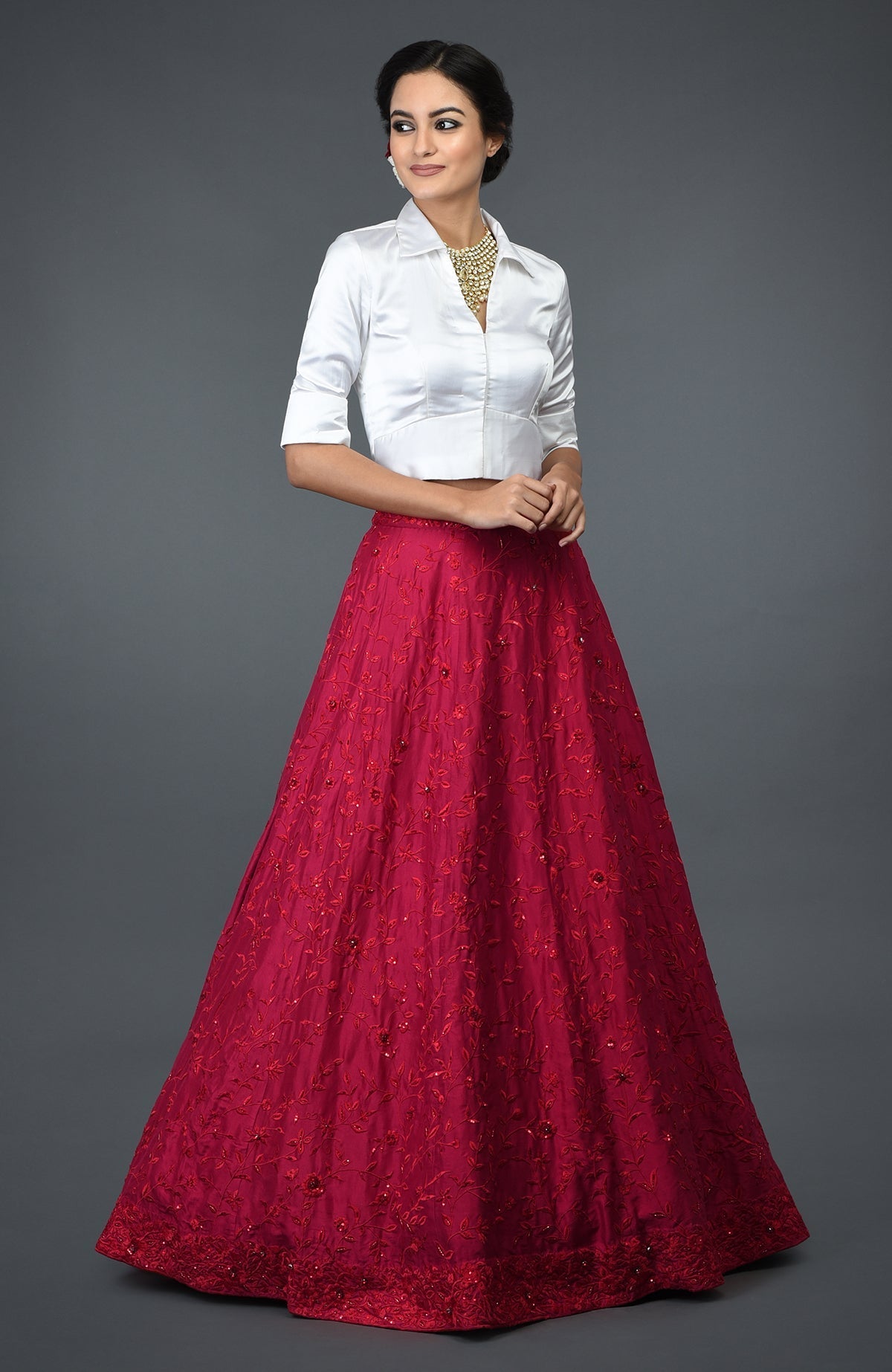 A woman models a red floral embroidered skirt with a white satin shirt blouse.