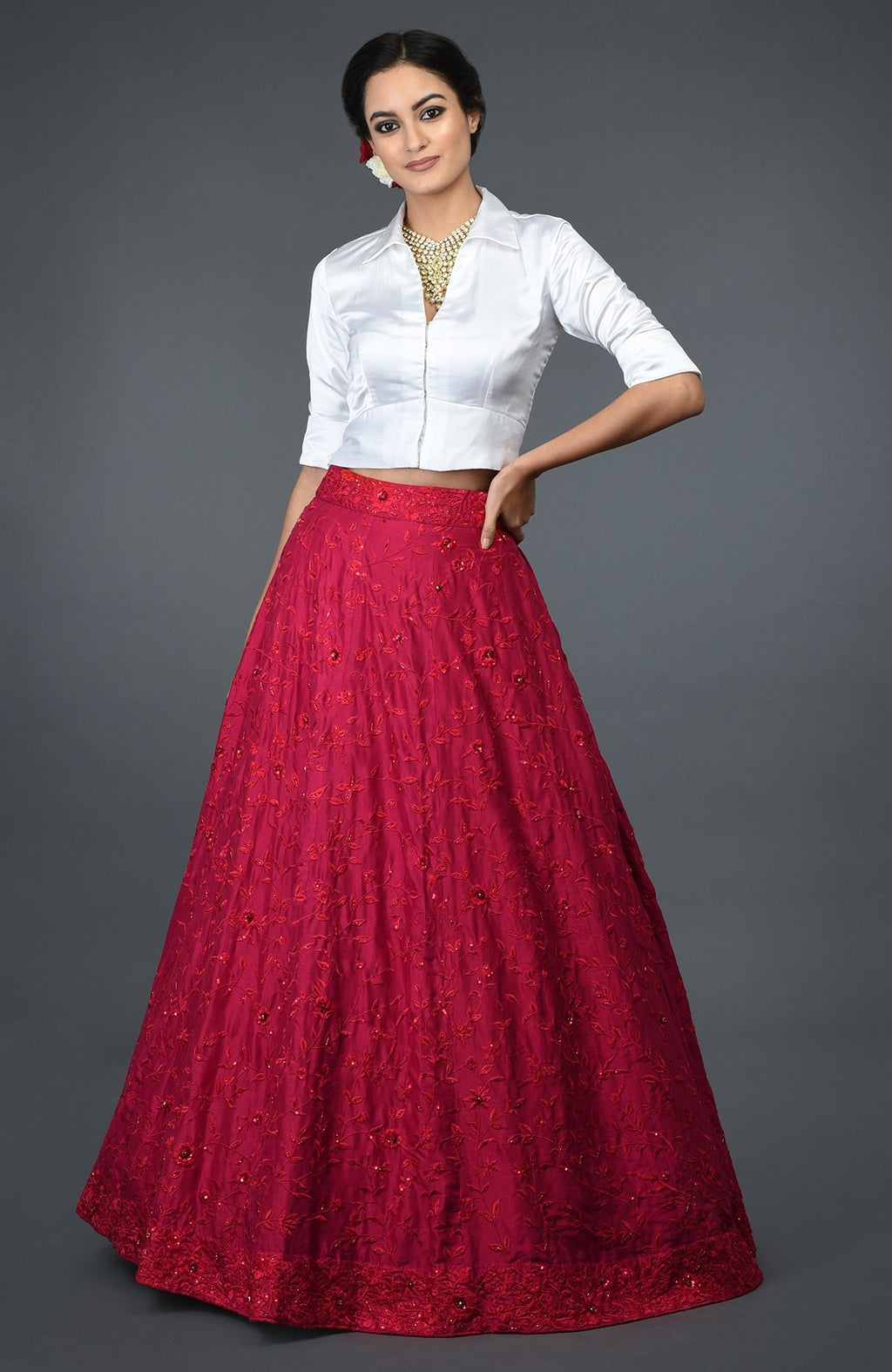 A woman models a red floral embroidered skirt and a white satin blouse.