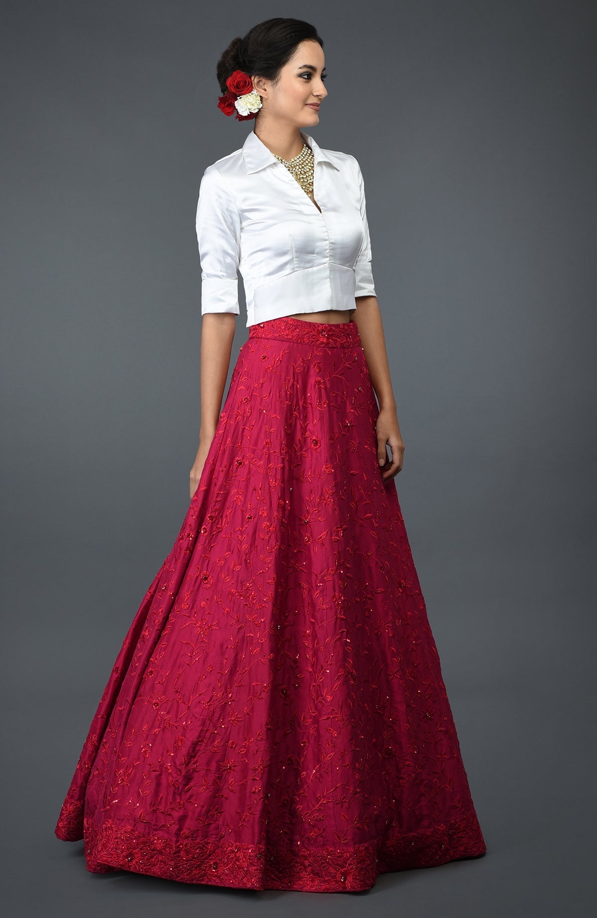 A woman models a red floral embroidered skirt and a white satin blouse.
