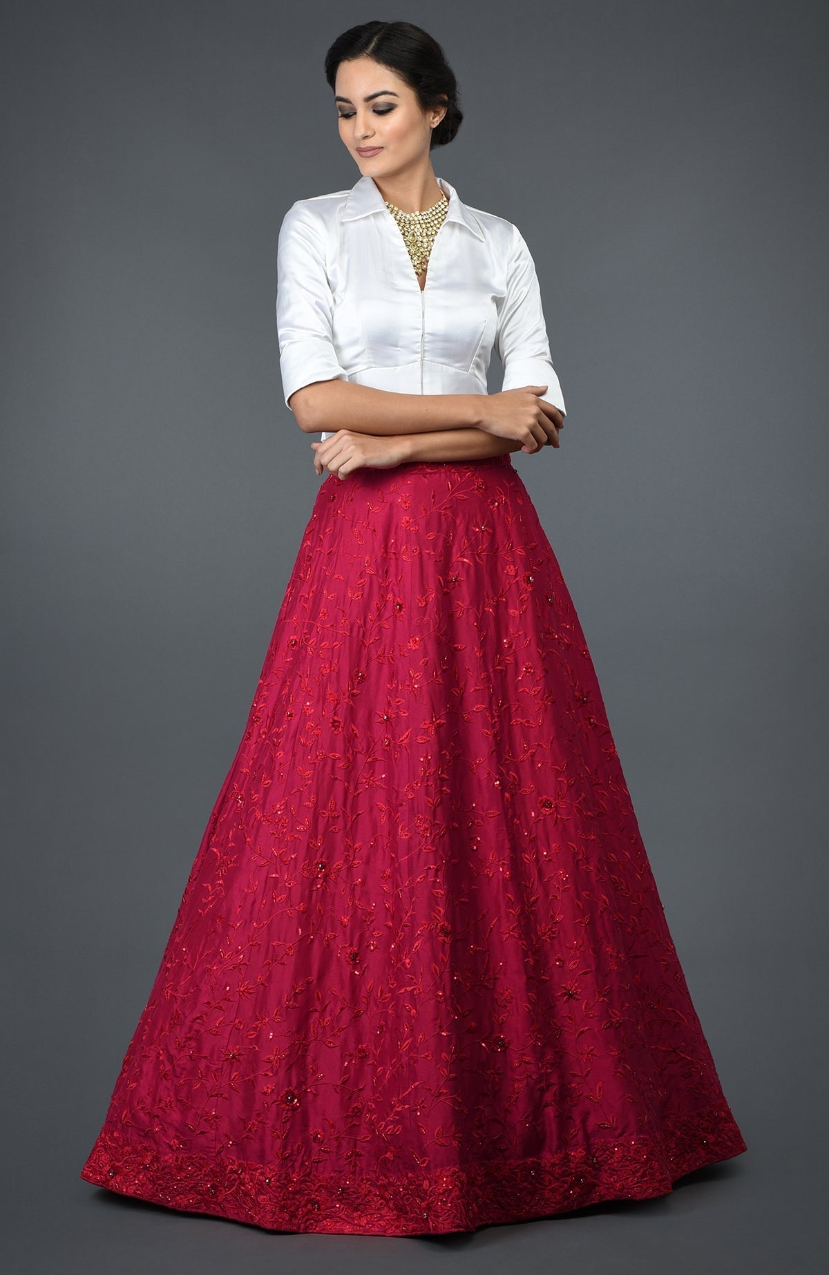A woman models a red floral embroidered skirt and a white collared blouse.