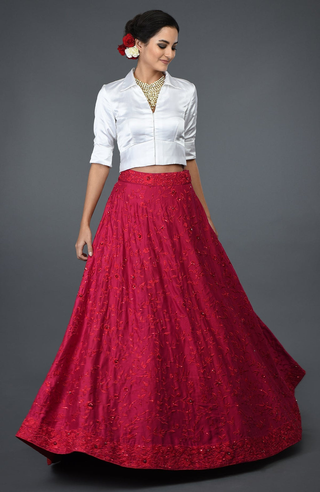 A woman models a red floral embroidered skirt with a white collared blouse.