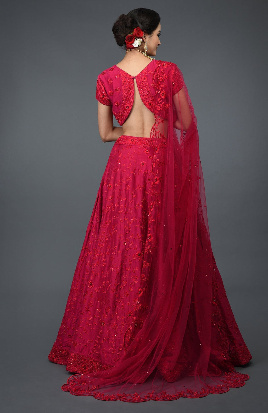 A woman from behind wearing a red floral embroidered lehenga with an open-back blouse.