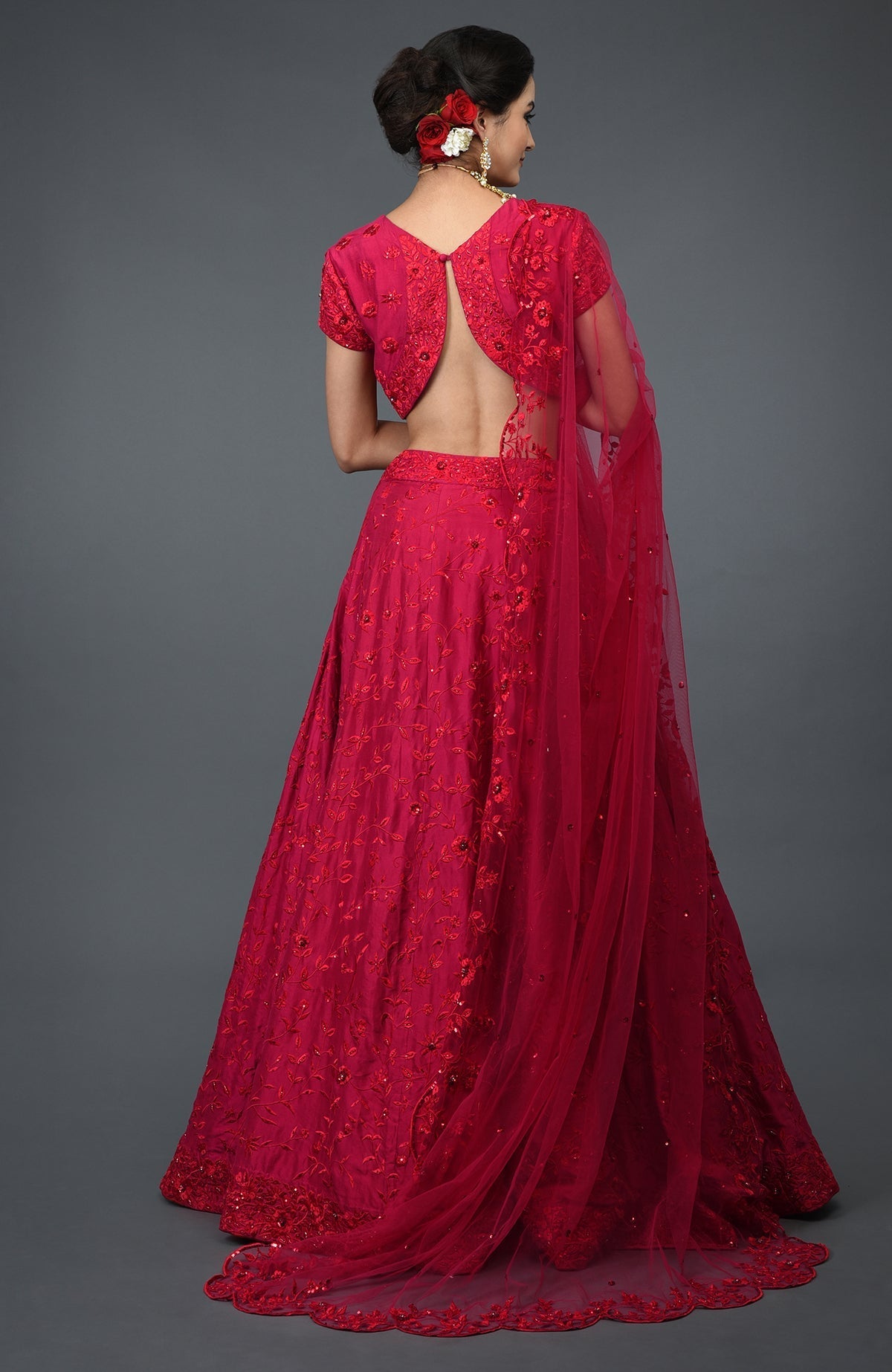 A woman from behind wearing a red floral embroidered lehenga with an open-back blouse.