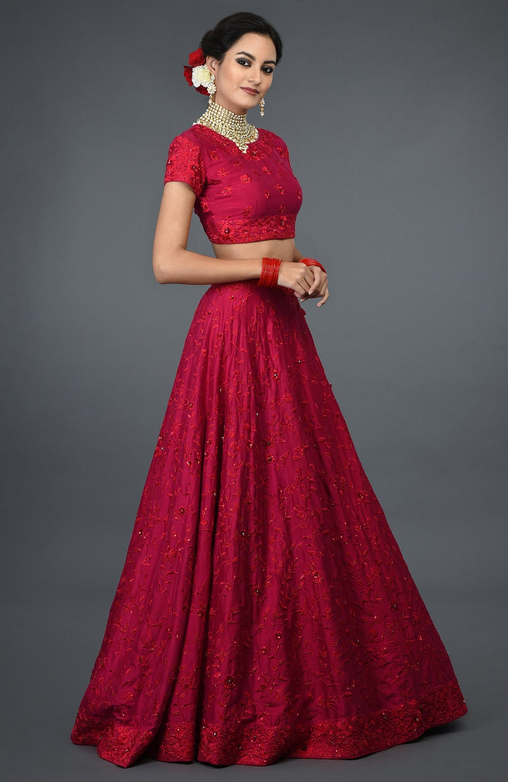 A woman models a red floral embroidered lehenga with a matching crop top and bangles.