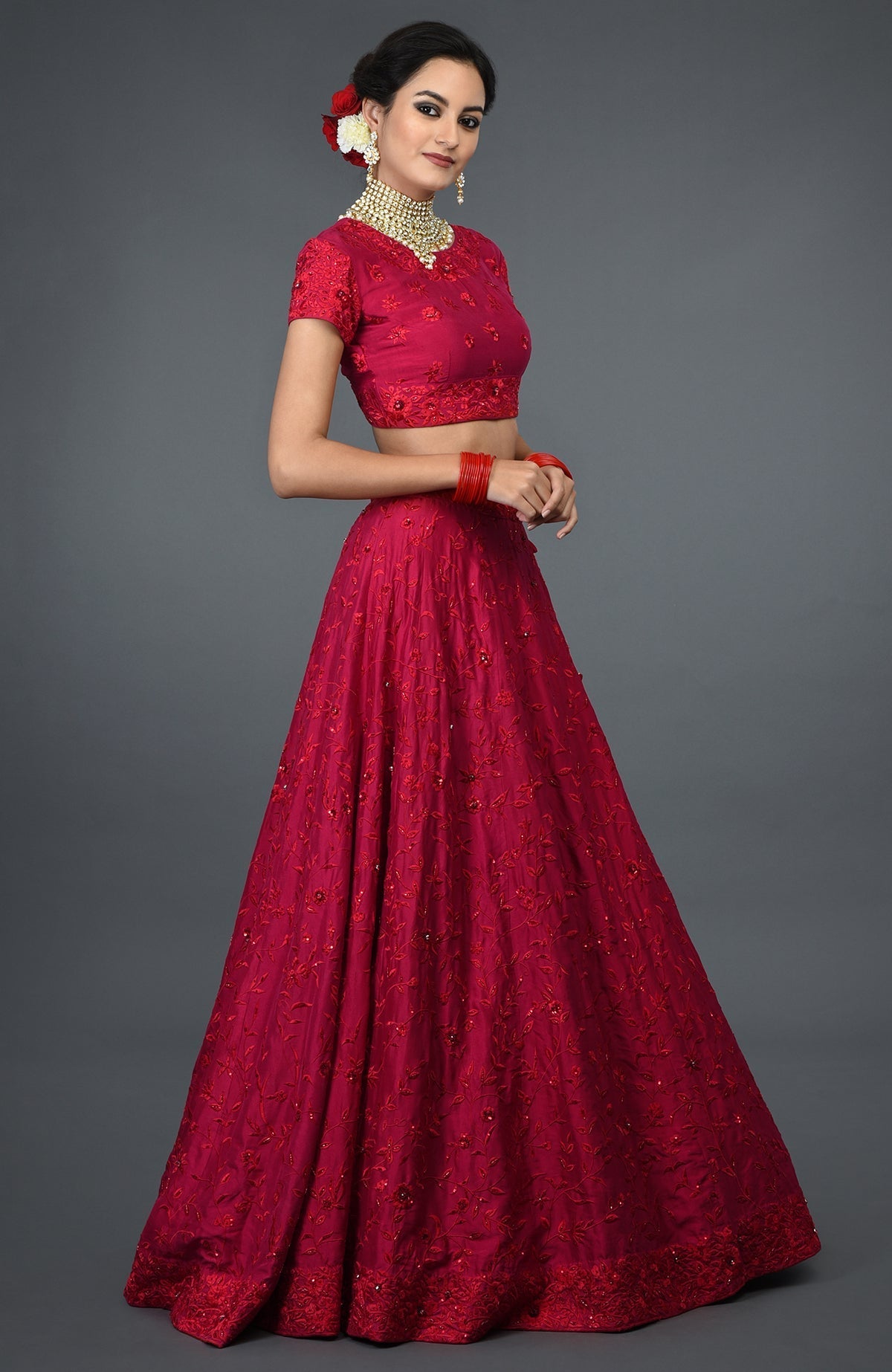 A woman models a red floral embroidered lehenga with a matching crop top and bangles.