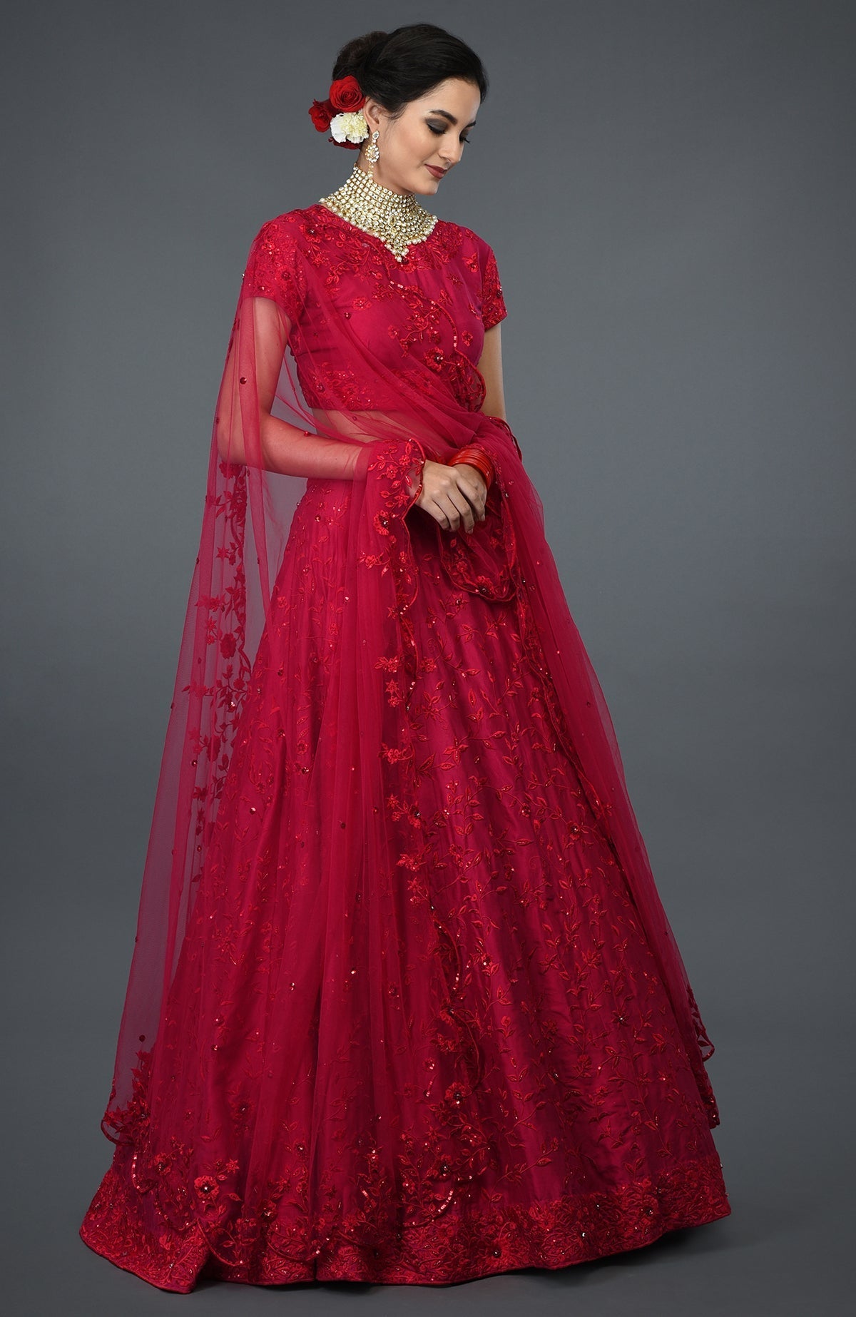 Woman in a red floral embroidered lehenga with a gold choker necklace.