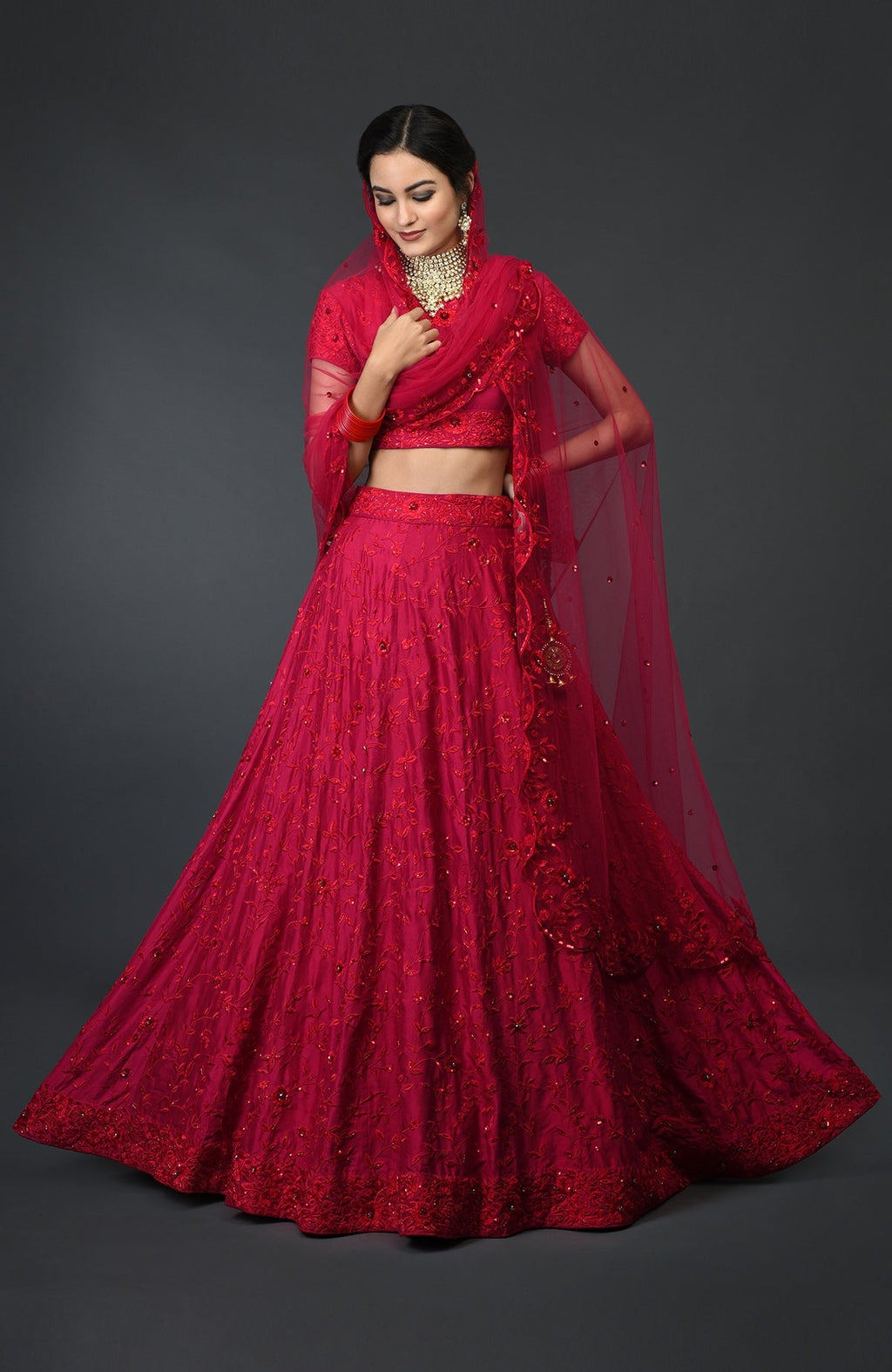 A woman models a red floral resham, sequin, and beads embroidered lehenga outfit.