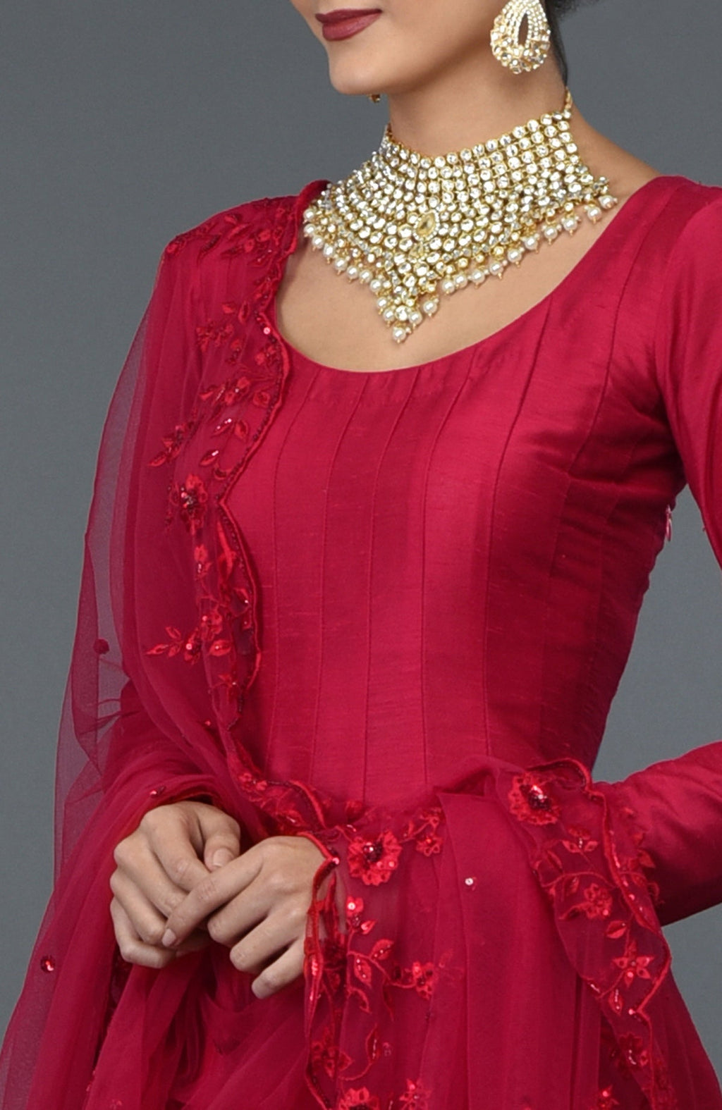 A woman in a red anarkali gown with floral embroidery and a pearl choker.