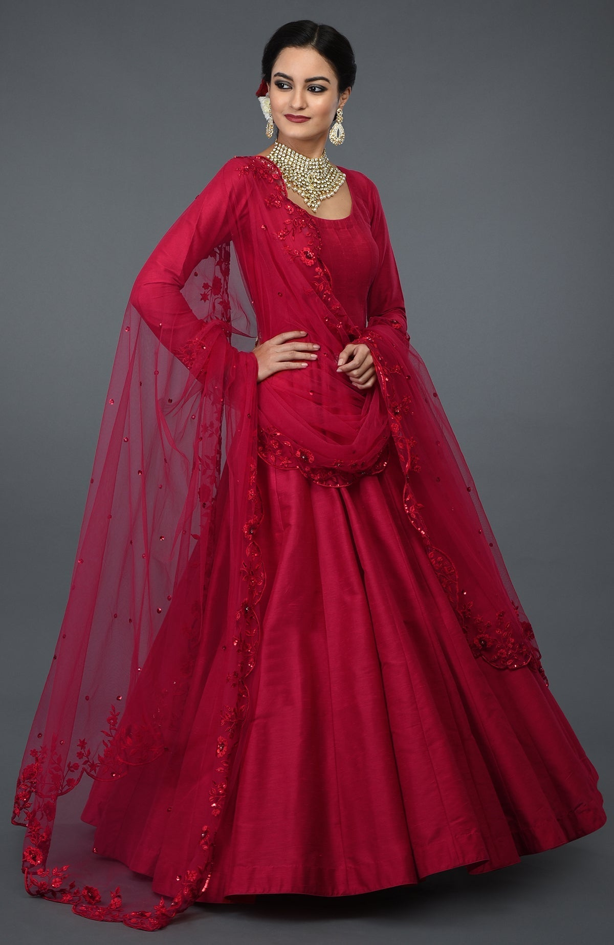 A woman models a red anarkali gown with floral embroidery and a sheer dupatta.
