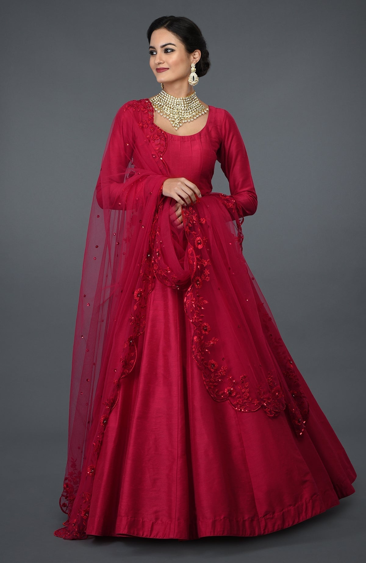 A woman models a red Anarkali gown with floral embroidery and a matching dupatta.