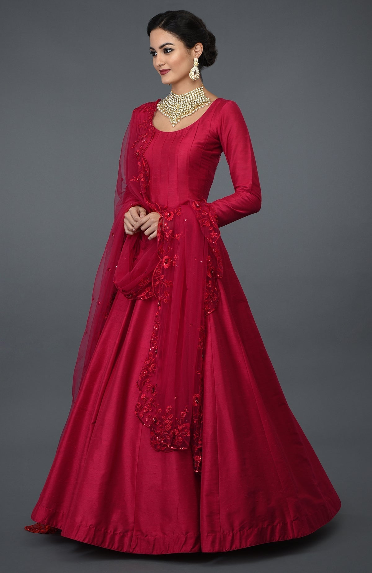 A woman models a red anarkali gown with floral embroidery and a matching dupatta.