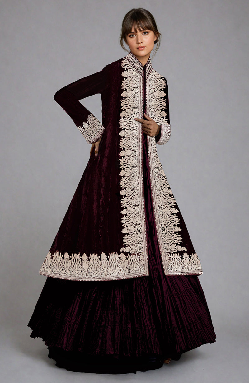 A model wears a maroon velvet jacket with silver embroidery over a matching skirt.
