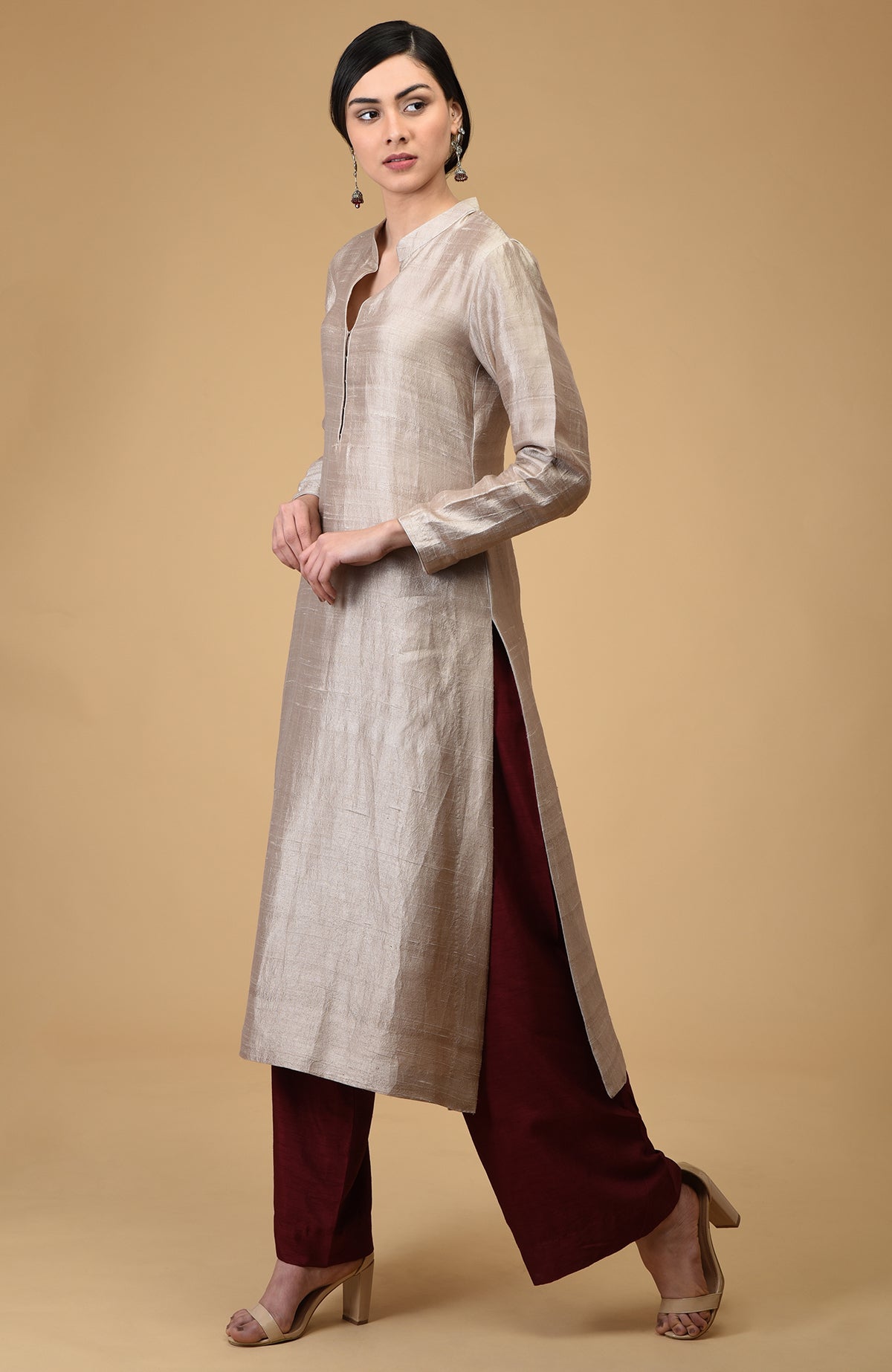 A woman models a beige raw silk kurta with maroon wide-leg pants and nude heels.