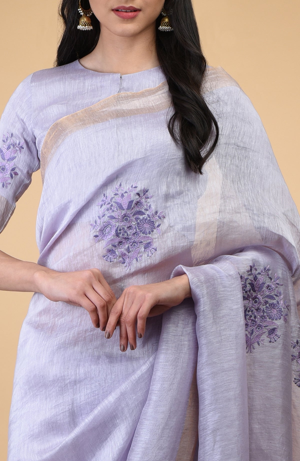 Lilac linen saree with floral embroidery and gold zari borders.
