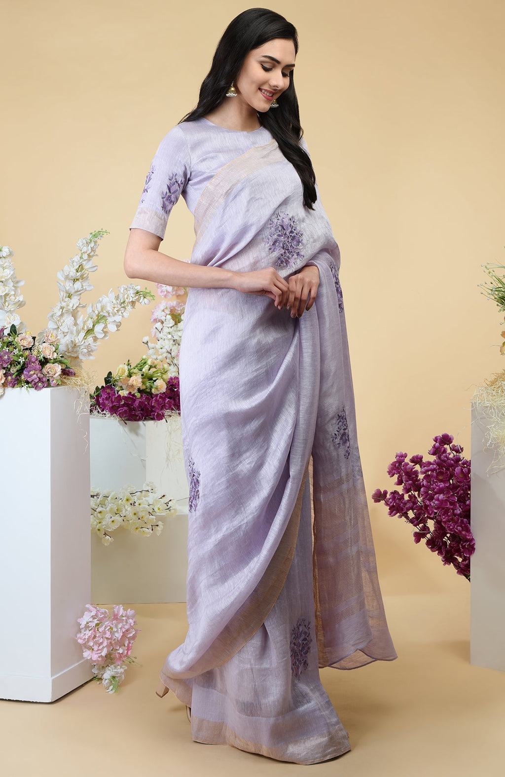 Lilac linen saree with floral embroidery and gold zari borders.