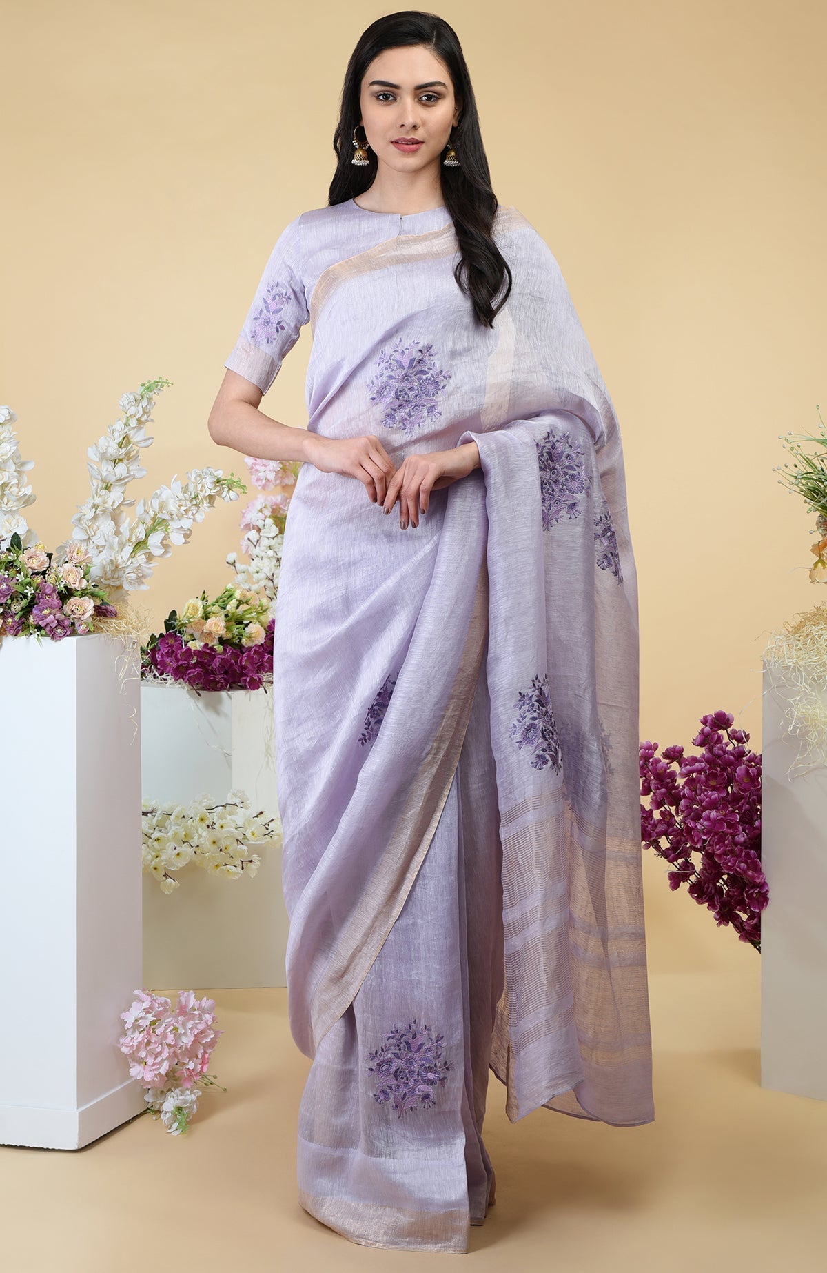 Lilac linen saree with floral embroidery and gold zari borders.