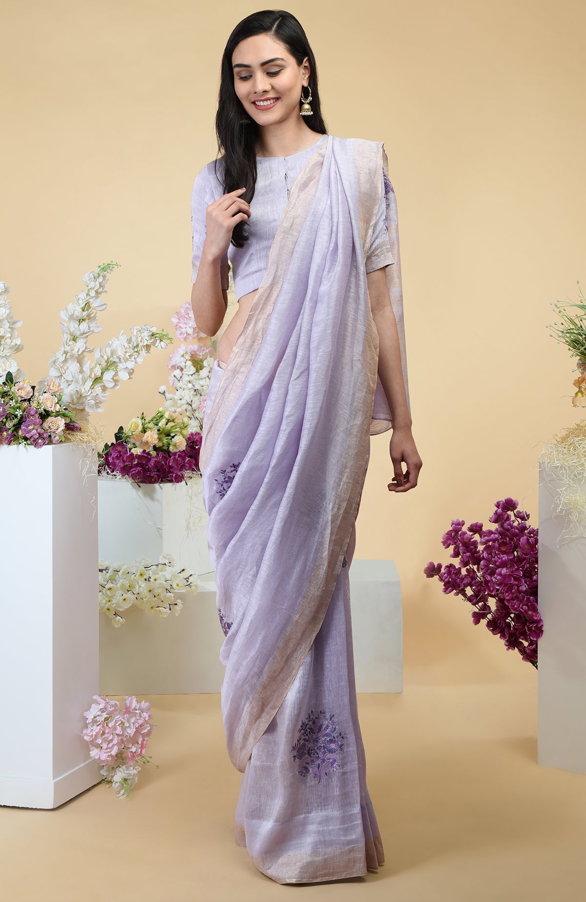 Lilac linen saree with floral embroidery and gold zari borders.
