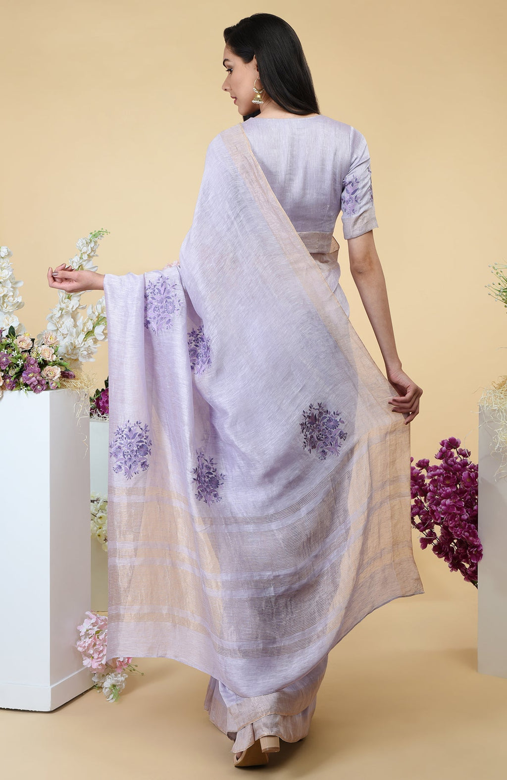 Lilac linen saree with floral embroidery and gold zari borders.