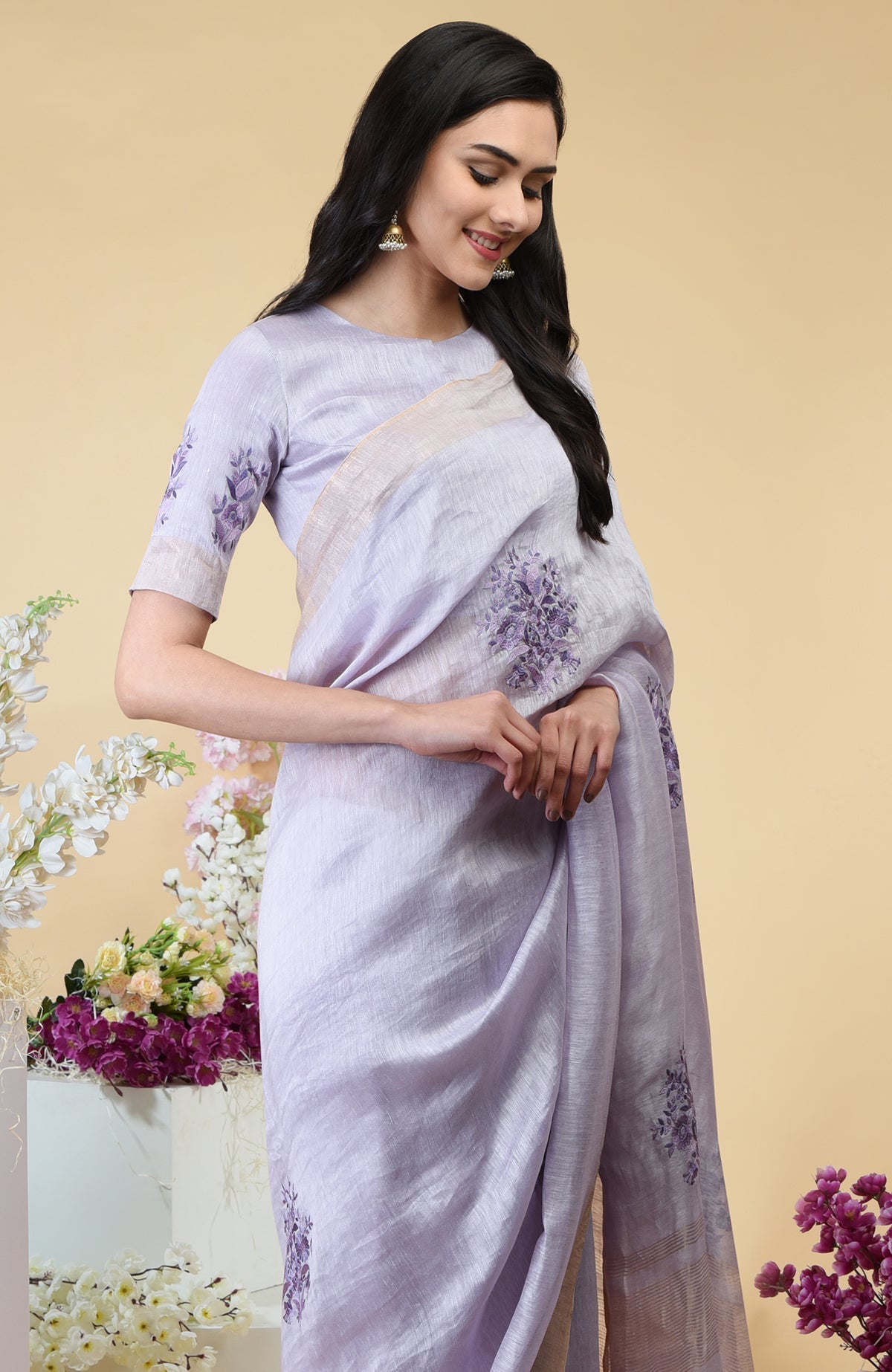 Lilac linen saree with floral embroidery and gold zari borders.