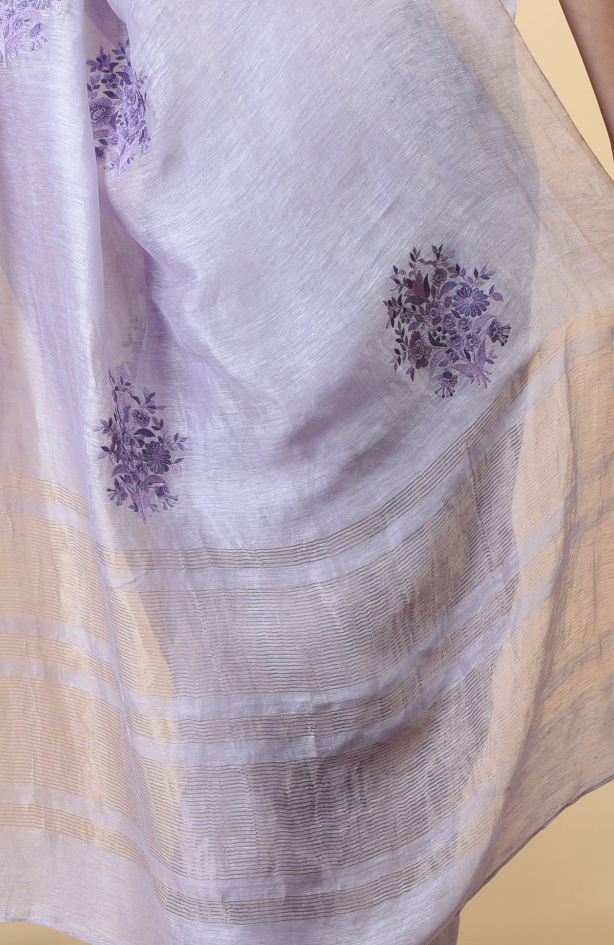 Lilac linen saree with purple floral embroidery and gold zari weave borders.