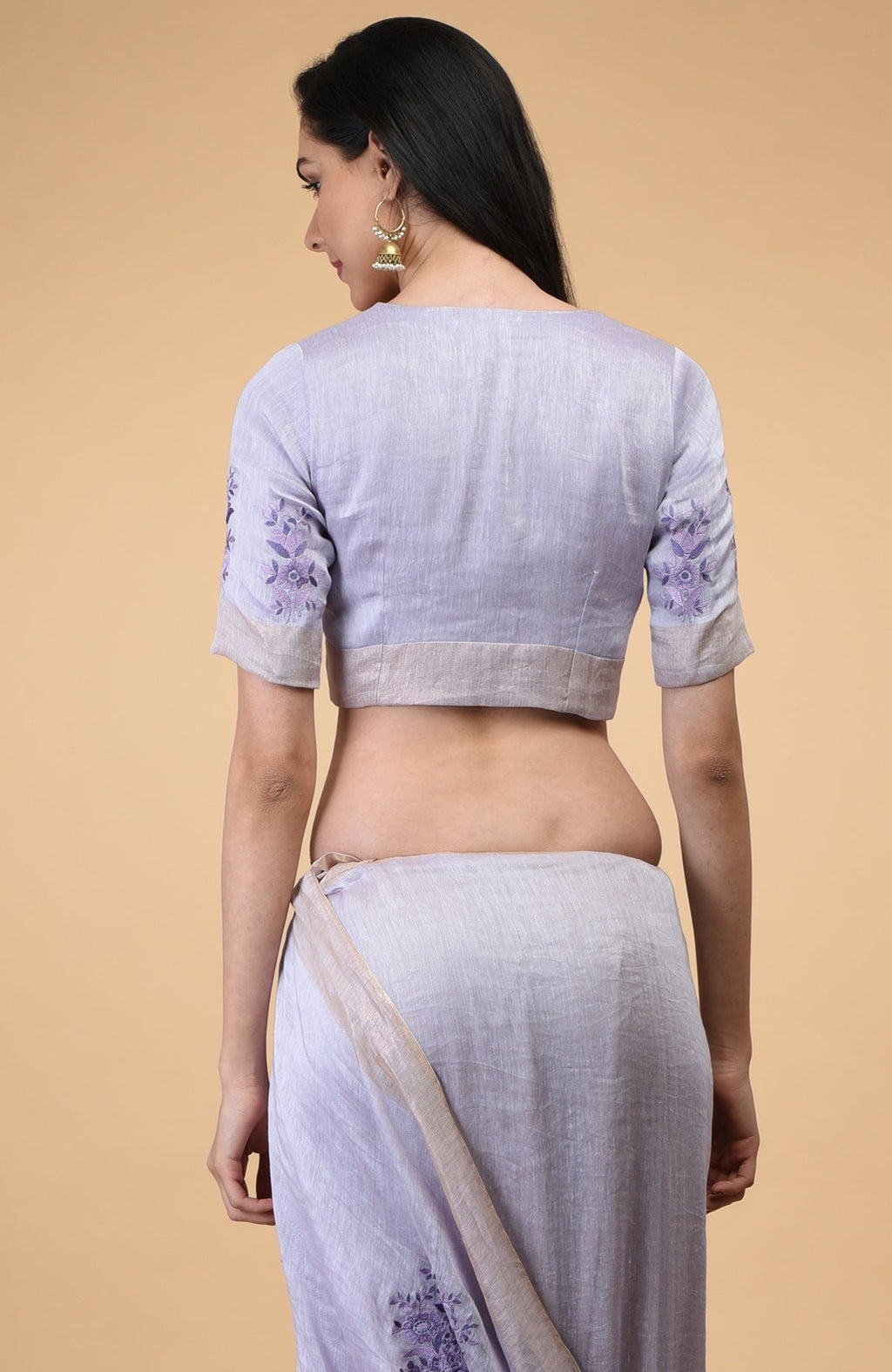 A woman from behind wears a lilac floral embroidered linen saree and matching blouse.