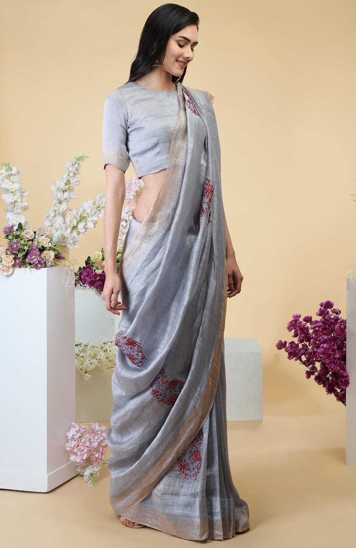 A woman models a dove grey linen saree with paisley embroidery and gold zari borders.