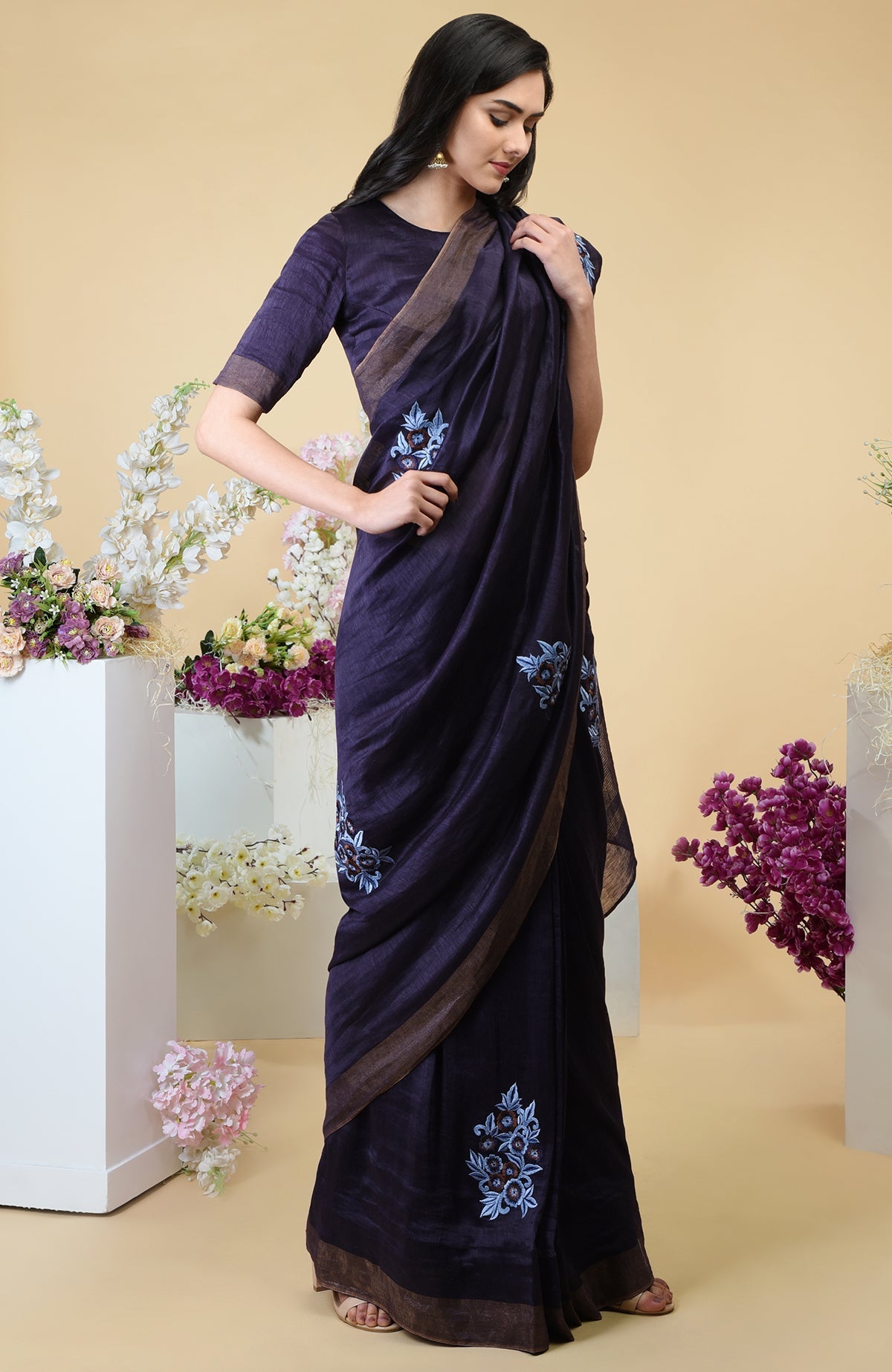 An eclipse blue linen saree with floral embroidery and gold zari borders.