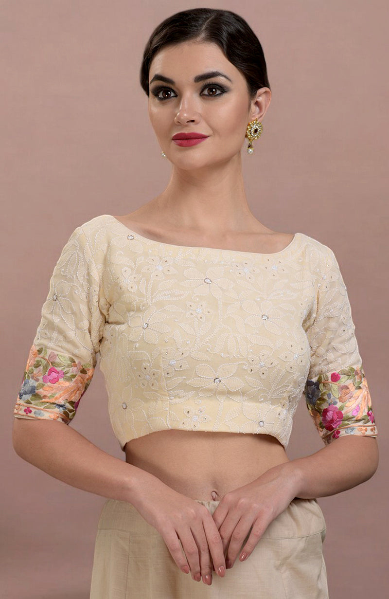 A woman models a champagne-colored blouse with intricate embroidery and floral sleeves.