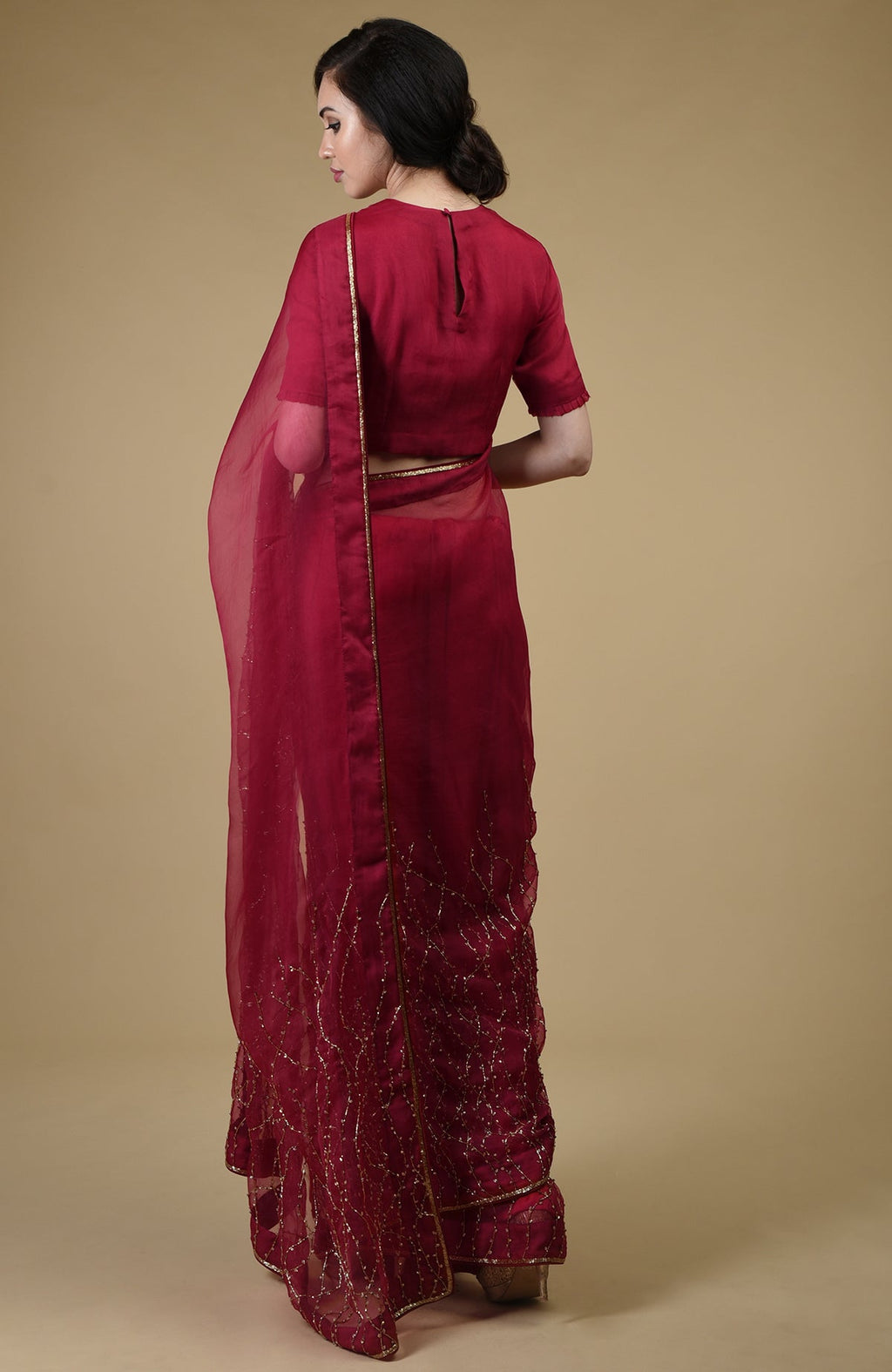 A woman from behind wears a red-gold embroidered saree with a matching blouse.