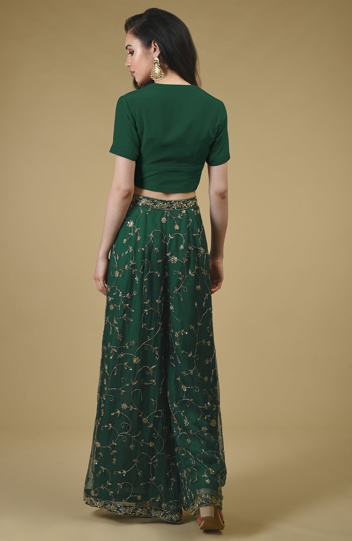 Rear view of a woman in an emerald green sharara suit with gold embroidery.