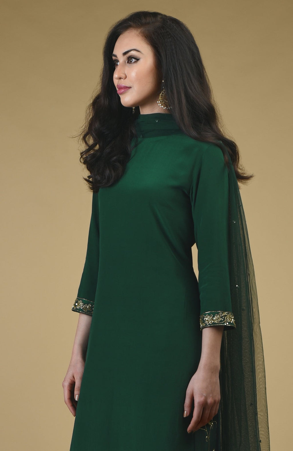 An emerald green sharara suit with gold zardozi embroidery on the sleeves.