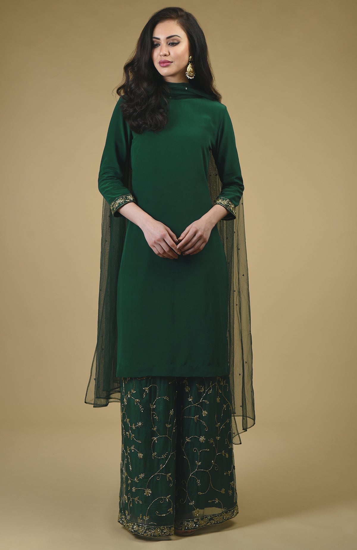 An emerald green sharara suit with gold embroidery and a sheer dupatta.