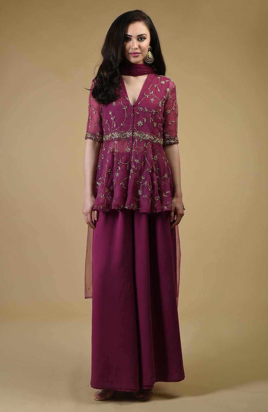 A woman models a peacock pink sharara suit with gold embroidery.