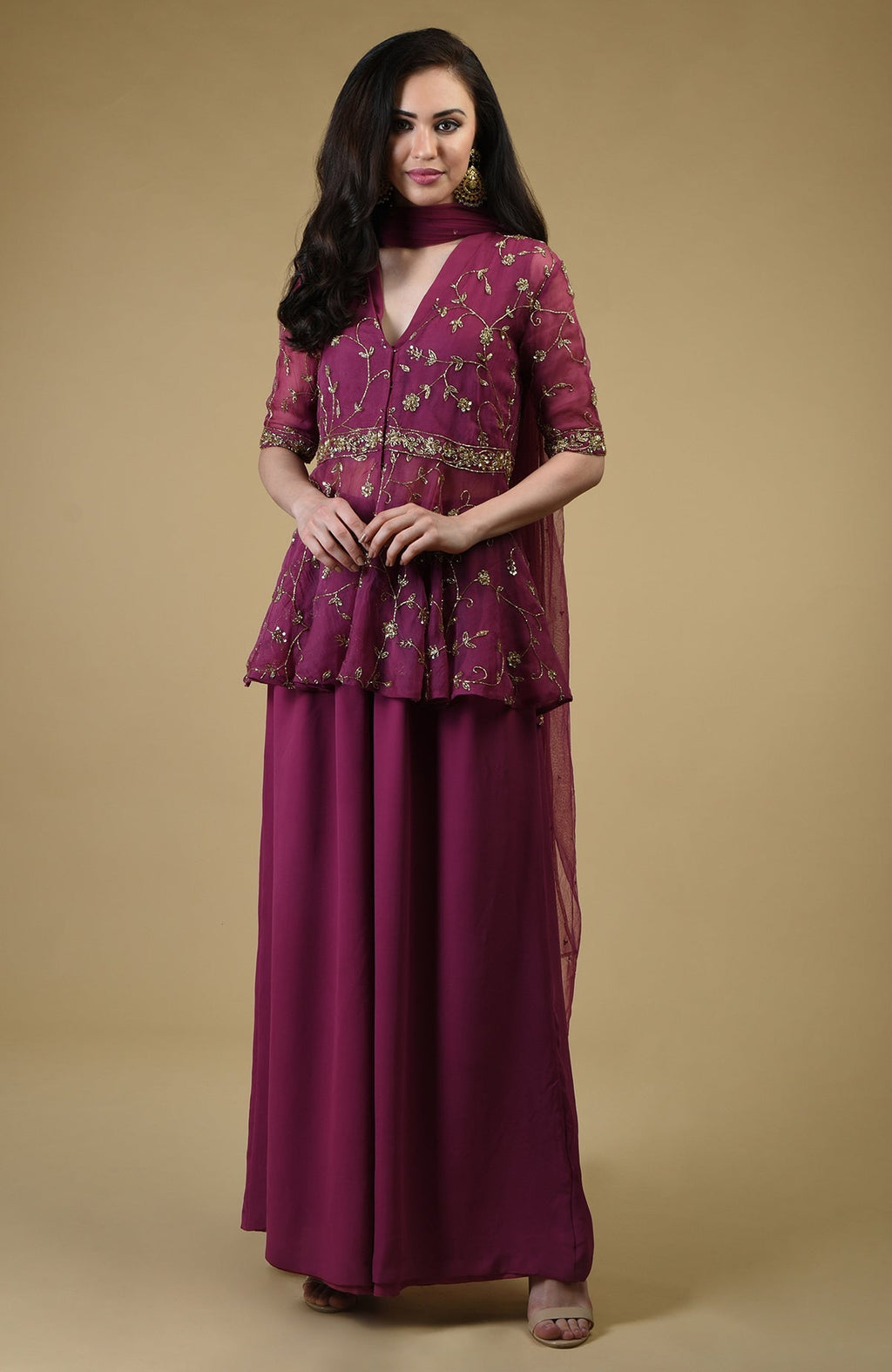 A woman models a peacock pink sharara suit with gold embroidery.