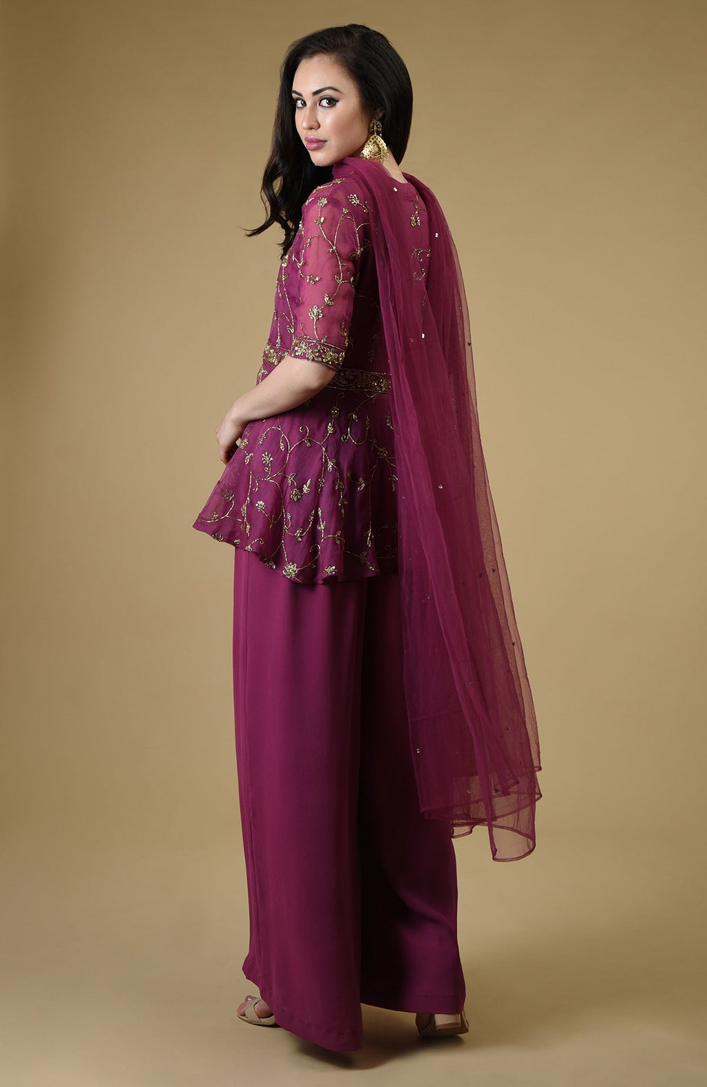 A woman models a peacock pink sharara suit with gold embroidery and a sheer dupatta.