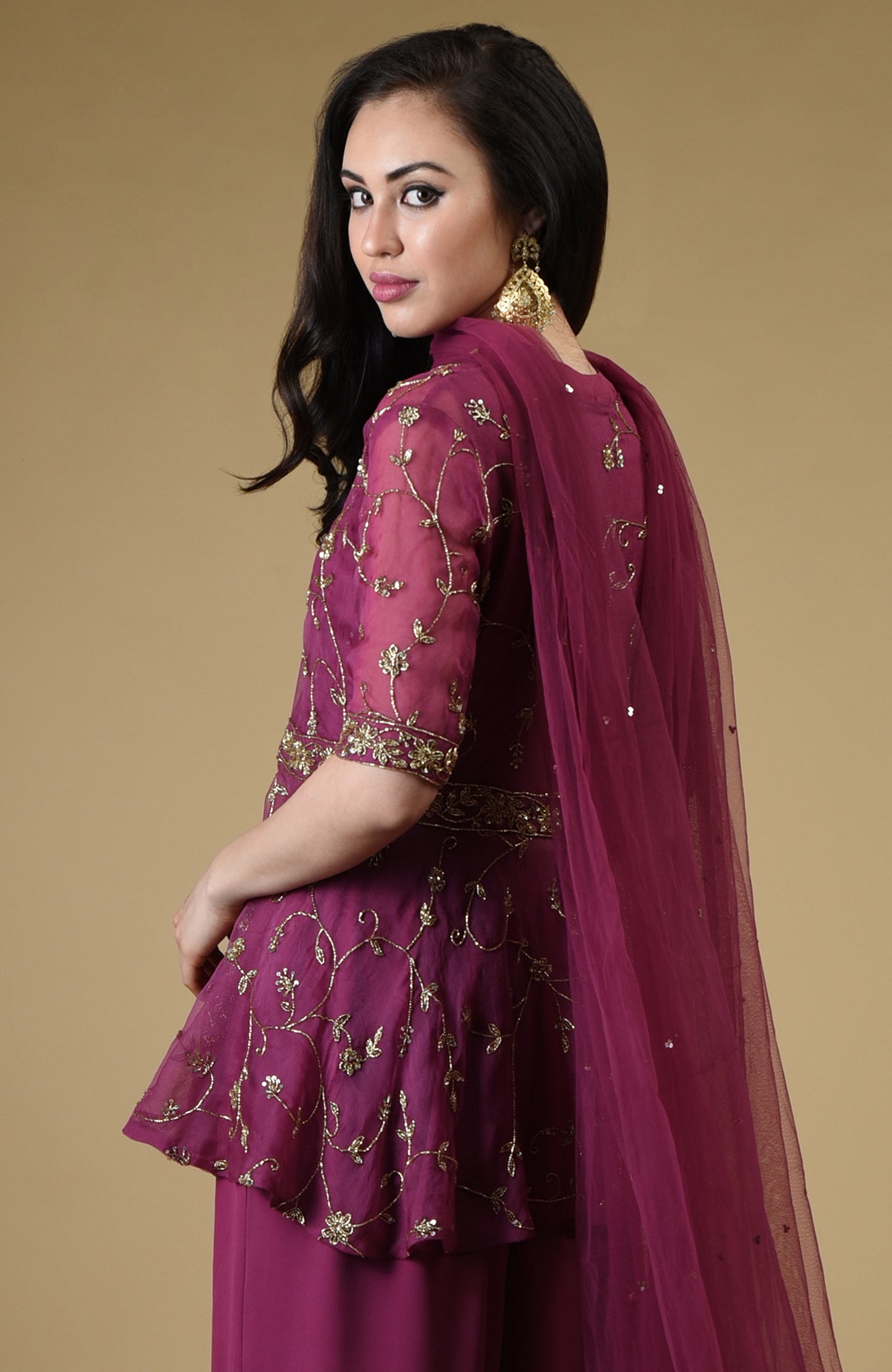 A woman models a peacock pink sharara suit with gold embroidery and a sheer dupatta.