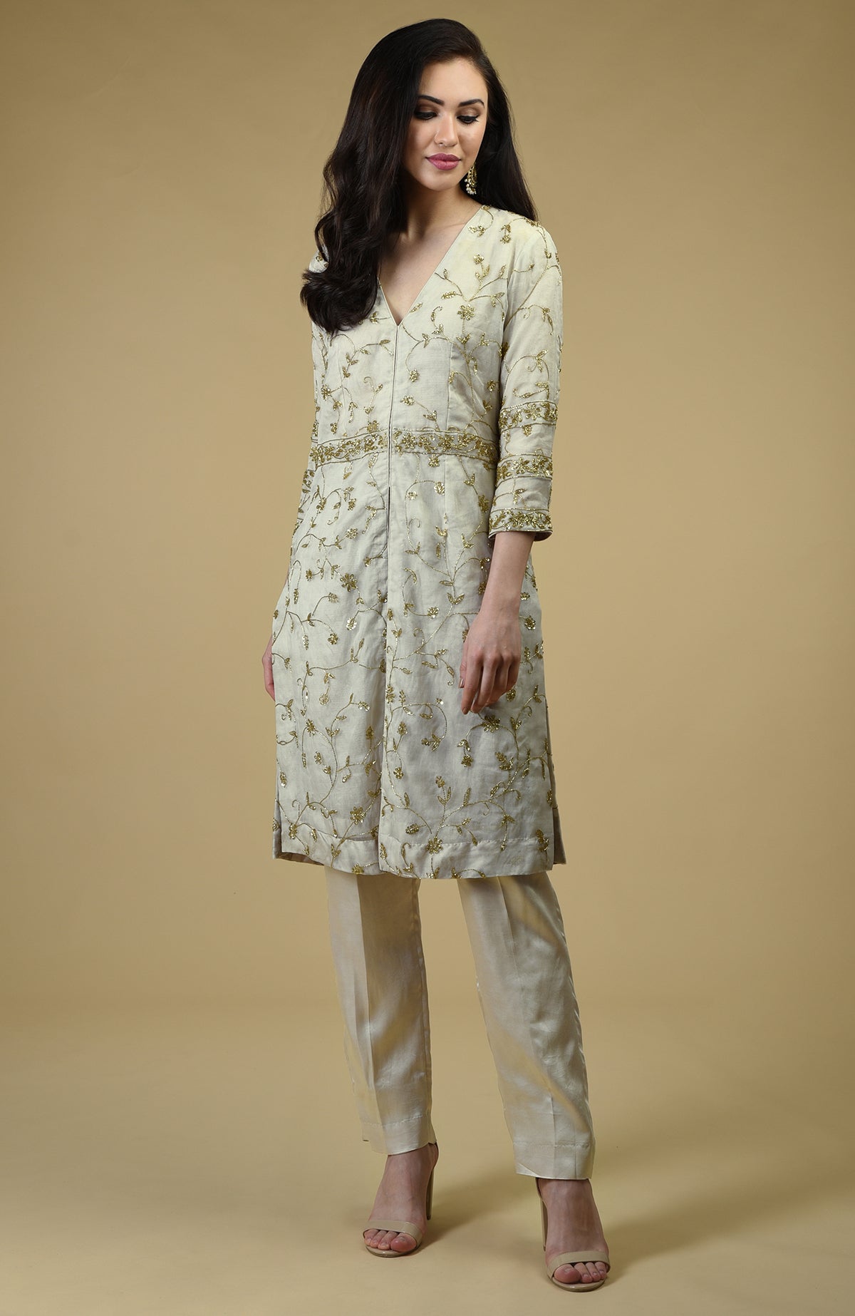 A woman models a white tunic and pants set with gold bead and zardozi embroidery.
