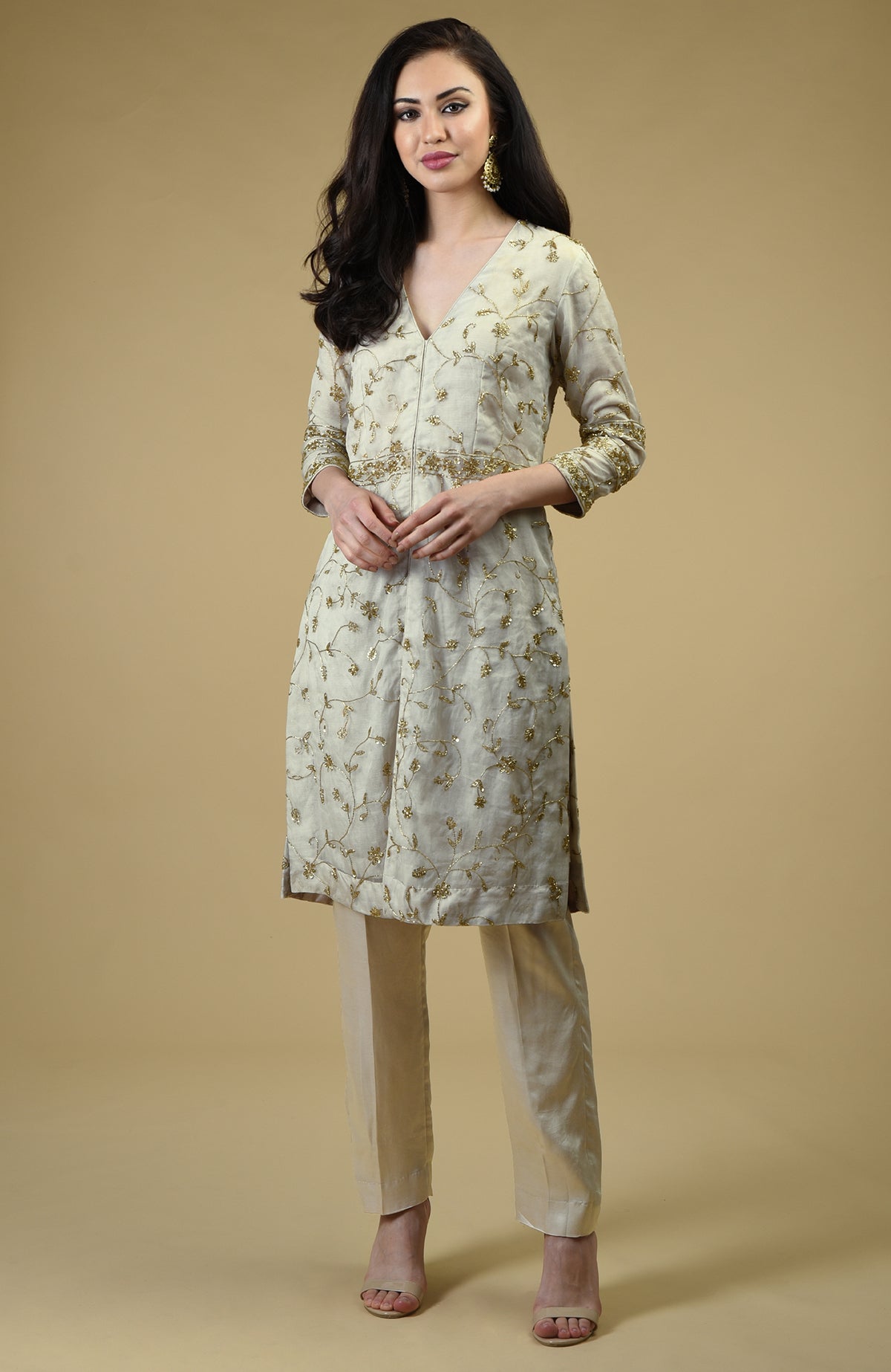 A woman models a white tunic with gold embroidery and matching pants.