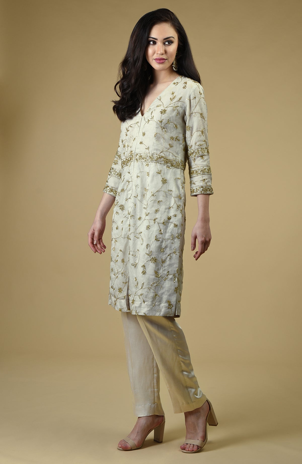 A woman models a white tunic and pants set with gold embroidery.