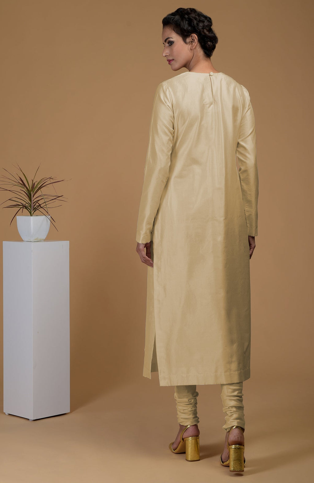 A woman models a beige pure Matka silk kurta set with a jewel neck and churidars.